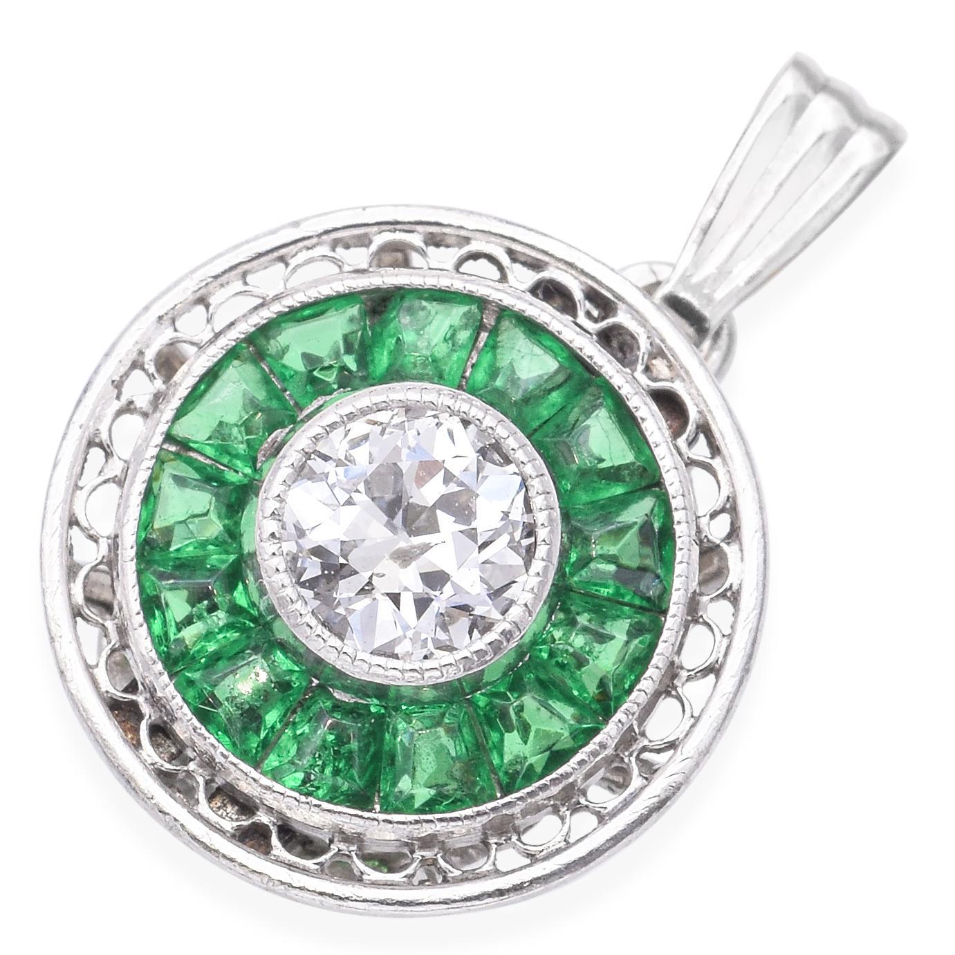 Pendentif élégant orné d'un diamant rond central de taille brillant, entouré de pierres précieuses d'un vert éclatant. Le design présente un travail filigrané complexe sur le bord extérieur, ajoutant une touche de sophistication. Le pendentif est