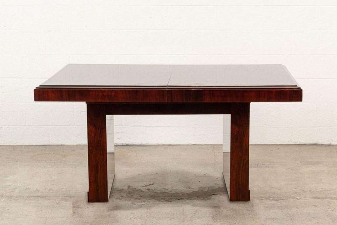 This exceptional antique French Art Deco walnut wood extendable dining room or conference room table is circa 1940. The table is hand-crafted from walnut wood in deep, rich mahogany tones with a lacquered finish. The table is incredibly well built