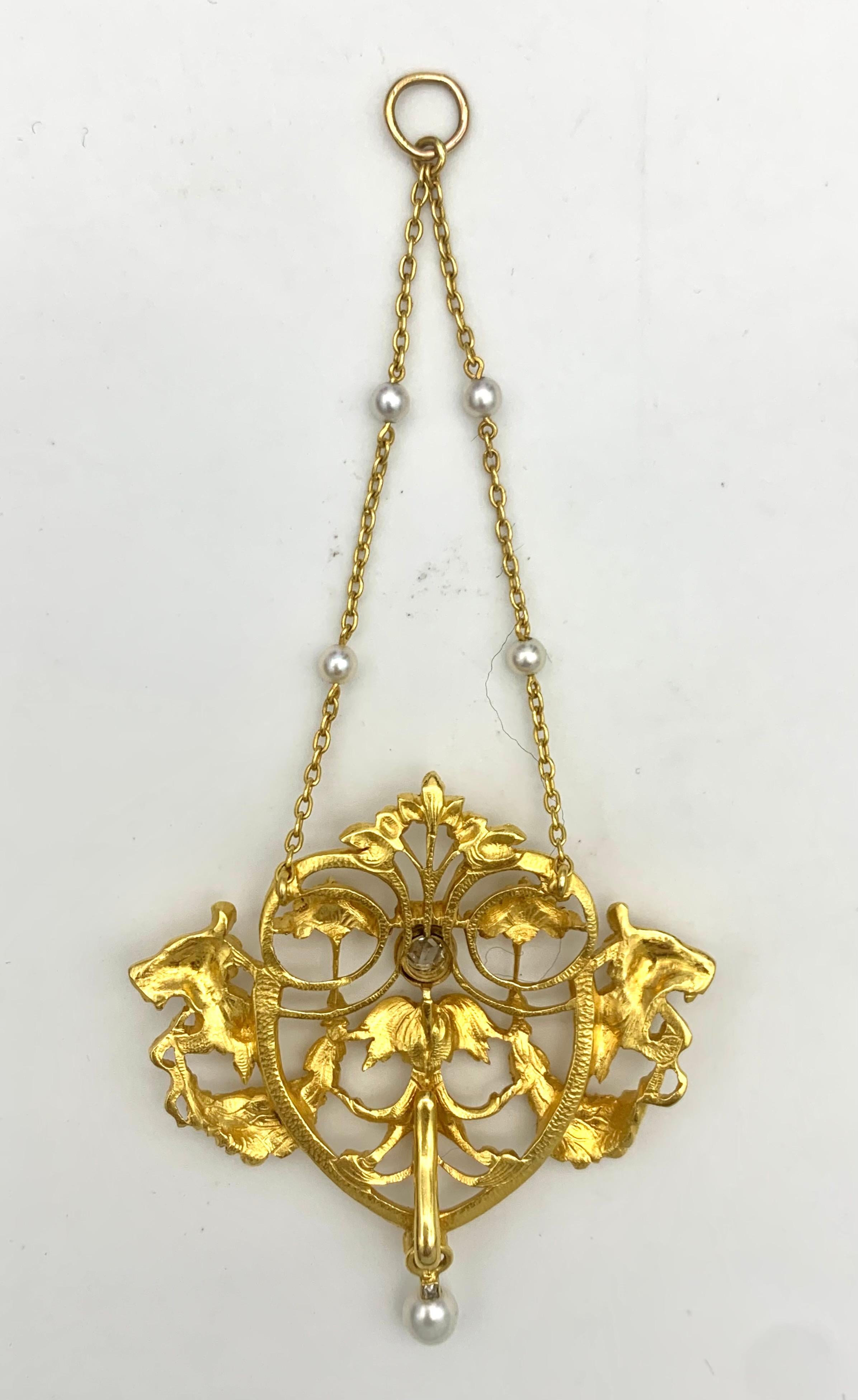 This elegant pendant has been made out 18 karat gold in the last decade of the 19th century. It is suspended from gold chains embellished with natural oriental pearls. The two lions heads in profile hold flower and fruit garlands in their mouth. The