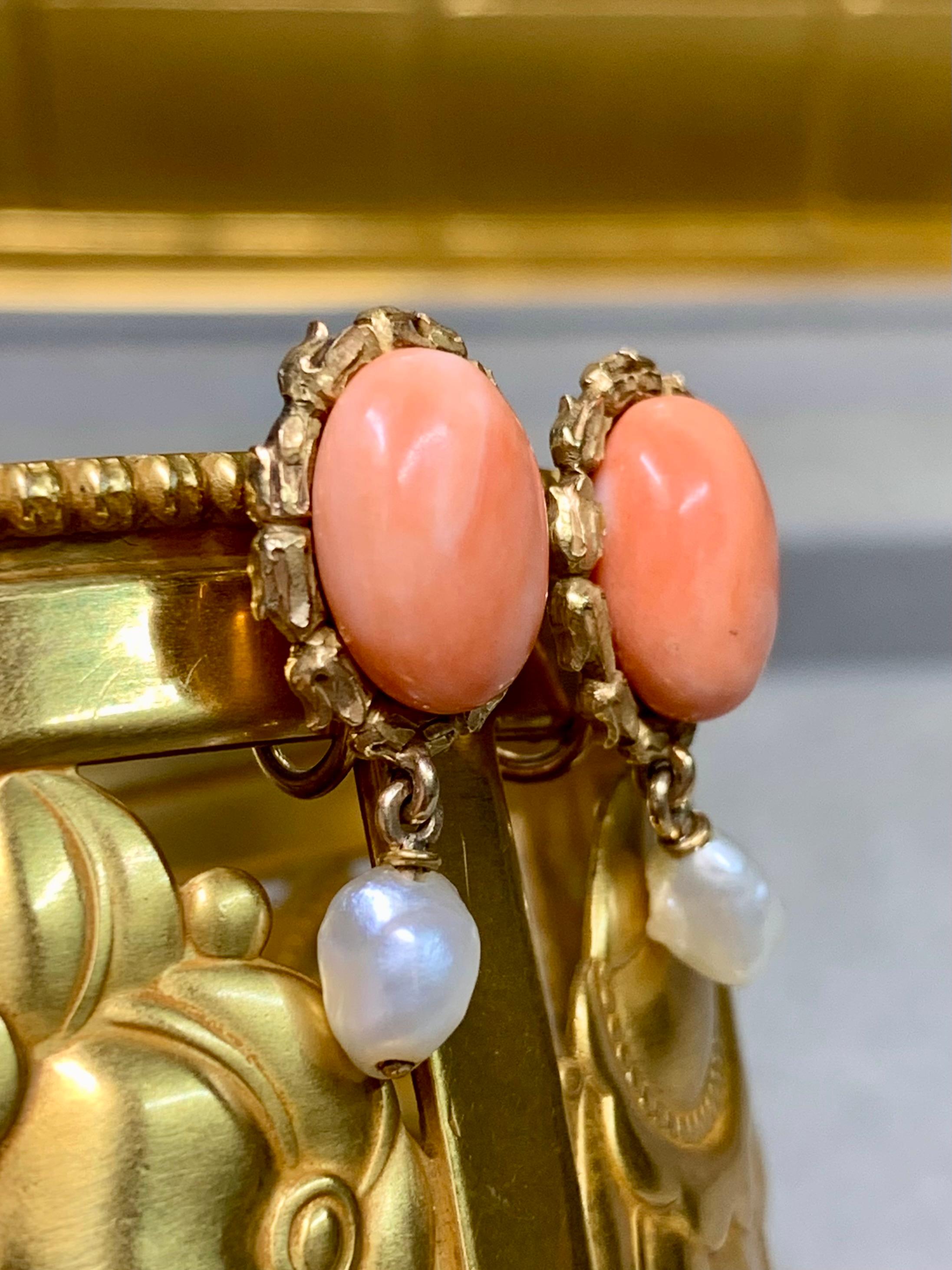 Un originale paio di antichi orecchini Art Nouveau, splendidamente realizzati in oro giallo 18 carati. Ogni orecchino presenta un contorno floreale intagliato che incornicia cabochon di corallo rosa naturale dai colori intensi. In basso sono sospese