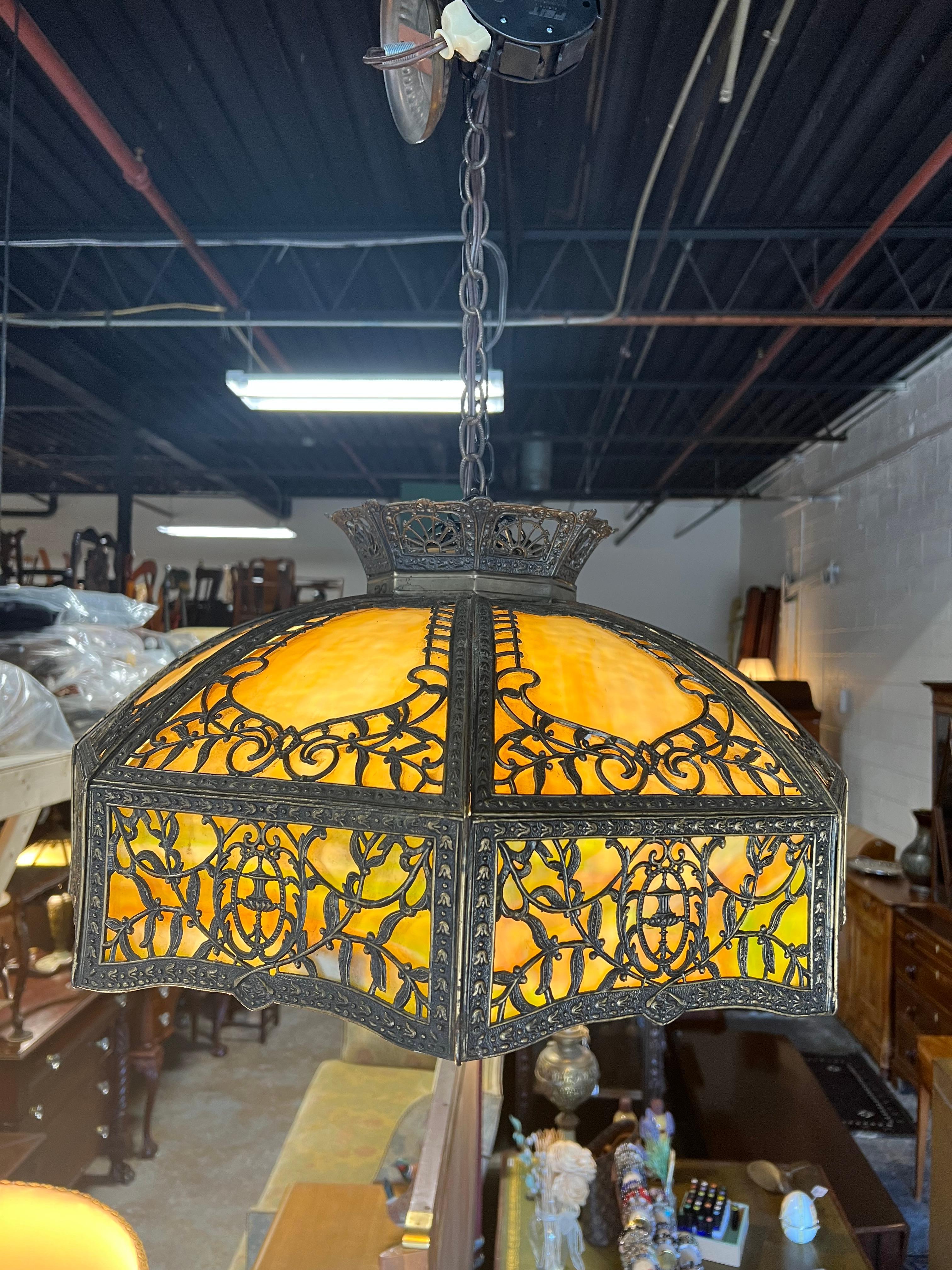 Questa antica lampada a sospensione, risalente al 1920 circa, è un bellissimo esempio di design dell'illuminazione in stile Art Nouveau. Il paralume è composto da vetro scoria riccamente colorato nei toni dell'ambra e del verde, che produce una luce