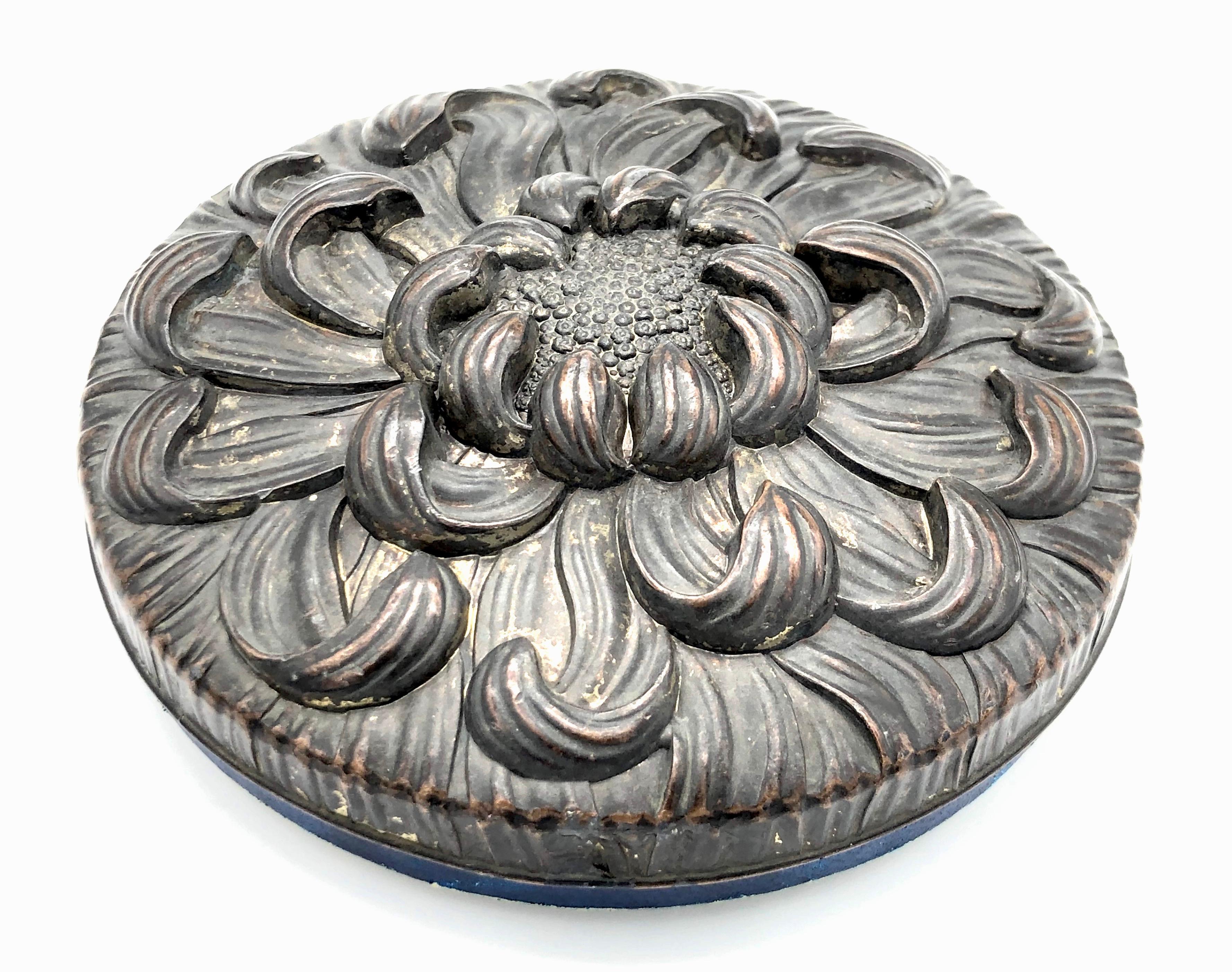 This stunning Art Nouveau gift box is executed in bronze and gold embossed blue leather. 
The round bronze lid is designed as a chrysanthemum and has a beautiful patina. The inside iof the cover is lined with dark blue velvet.
The leather