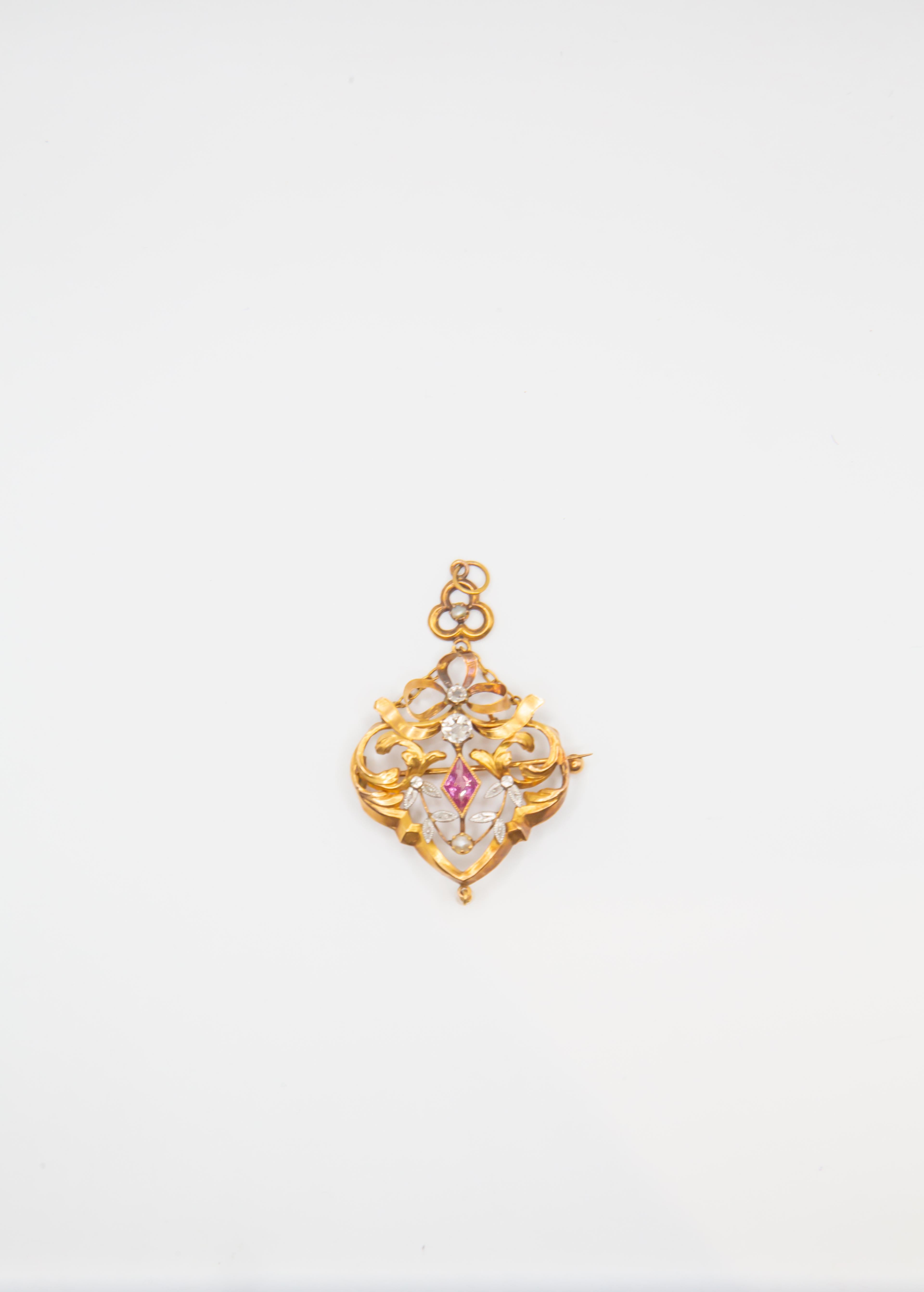 Una spilla d'epoca mozzafiato in stile Art Nouveau, realizzata in ricco oro giallo 14 carati, ornata da un vivido zaffiro rosa nel cuore, incorniciato da intricate volute e delicati accenti di diamante. Il design traforato evoca motivi botanici