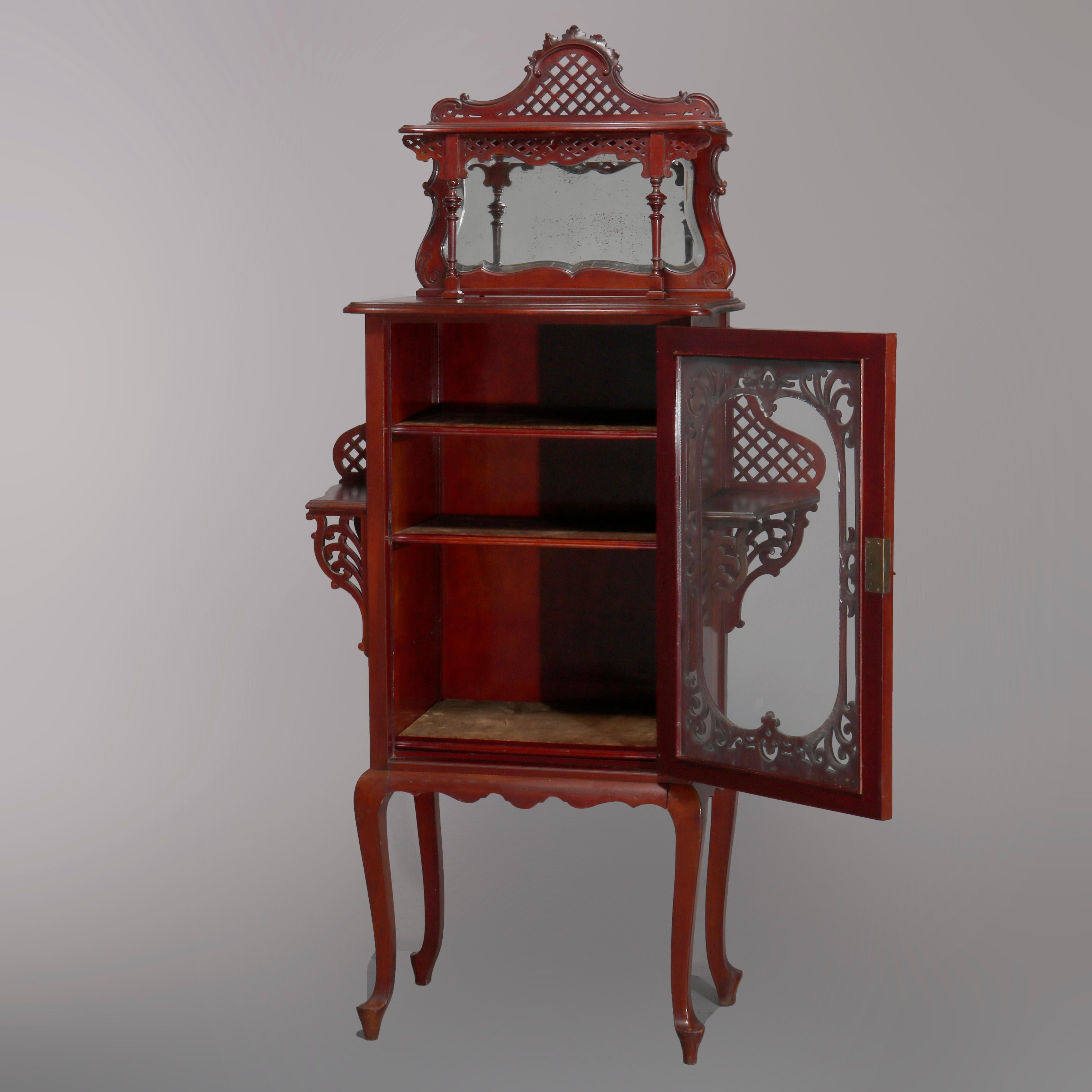 An antique Art Nouveau étagère offers mahogany construction with upper display over beveled mirror backsplash surmounting single door case having flanking display shelves, raised on cabriole legs, carved reticulated lattice, scroll and foliate