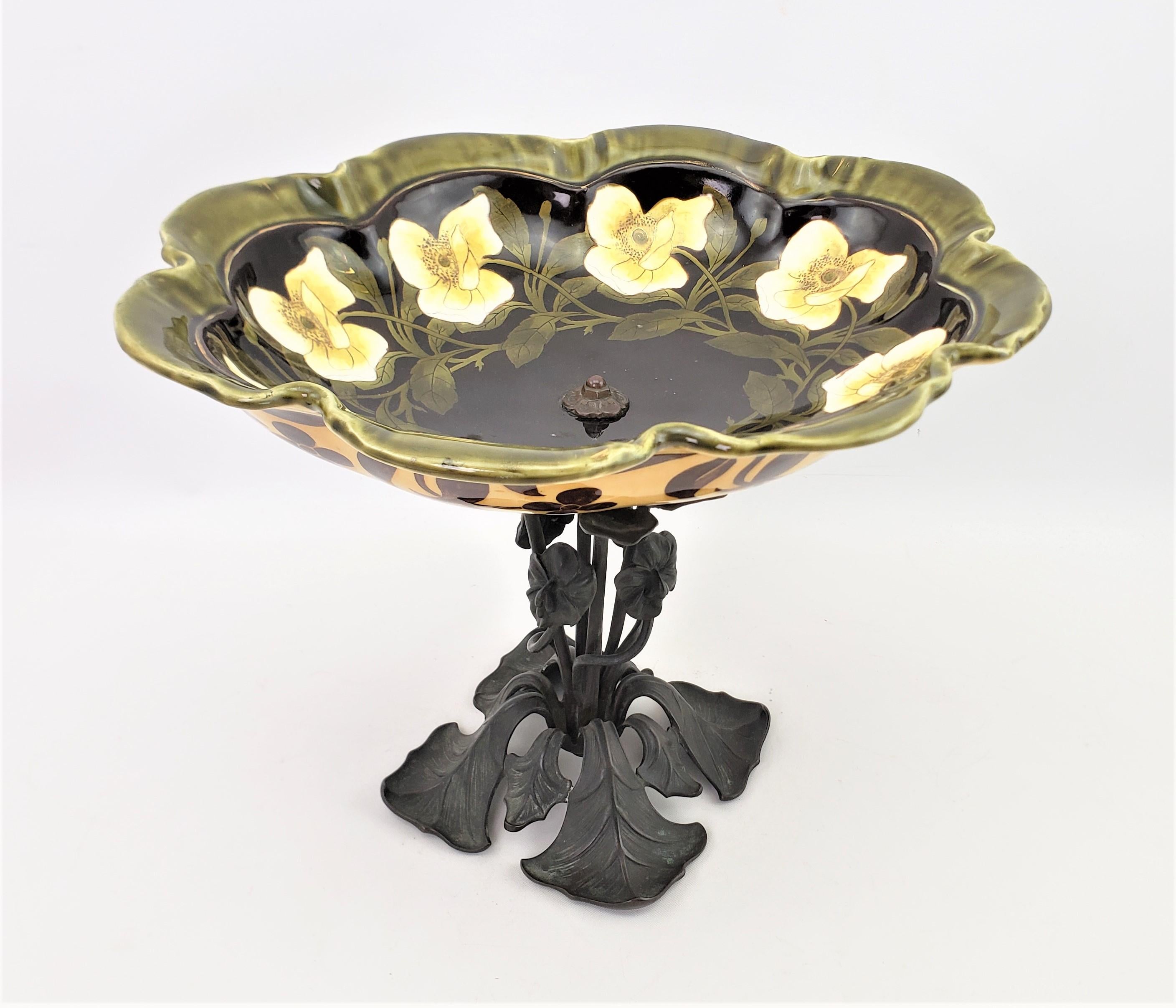 This antique cast bronze and ceramic pedestal bowl or centerpiece is unsigned, but presumed to originate from Austria and dating to approximately 1900 and done in the period Art Nouveau style. The bowl itself is done with an oval shape and scalloped