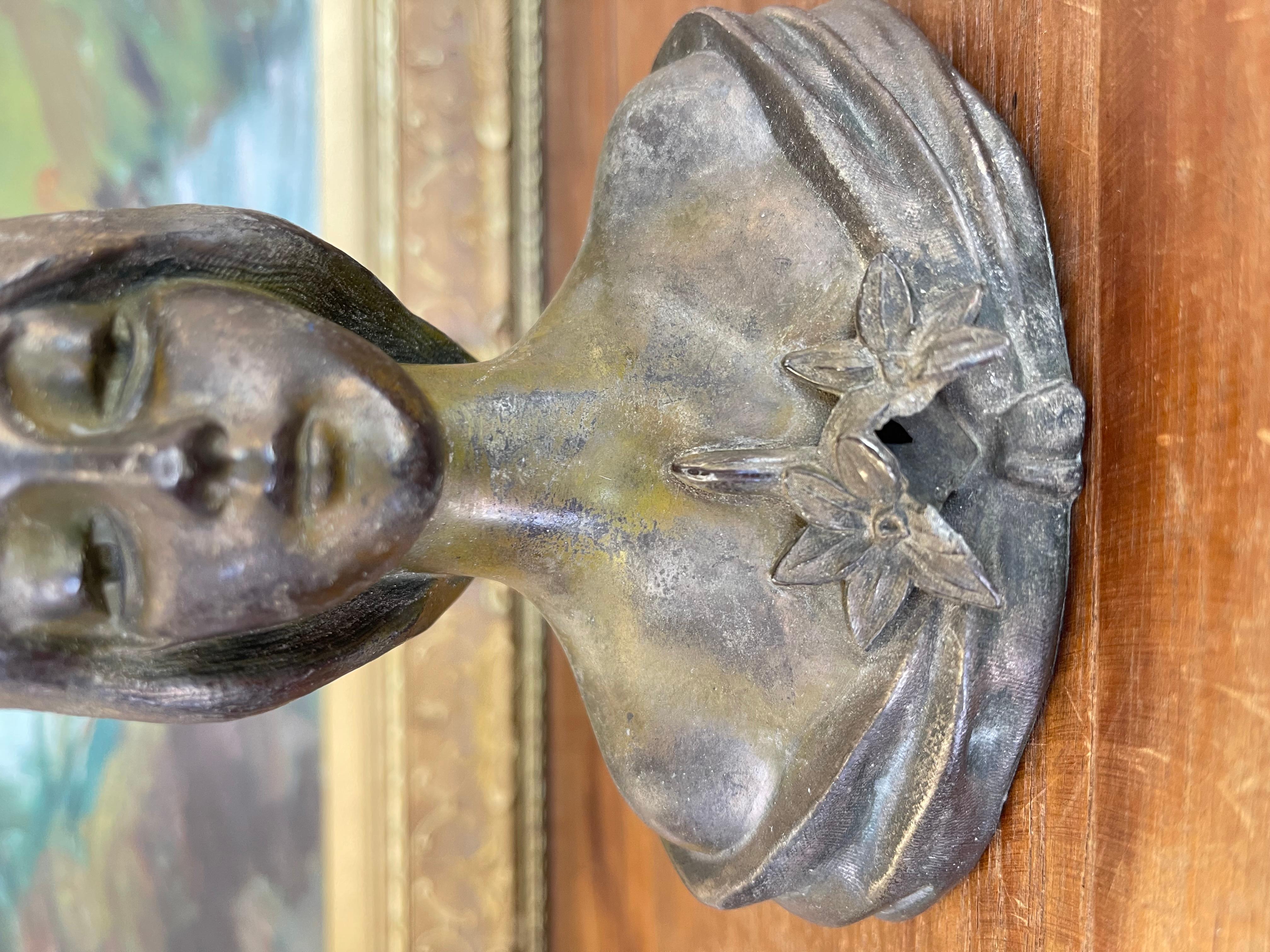 Buste en métal moulé Art nouveau du début du XXe siècle représentant une jeune femme sereine, ses cheveux encadrant doucement son visage. La figure est drapée dans un châle stylisé orné d'une paire de lys à l'encolure, un motif caractéristique des