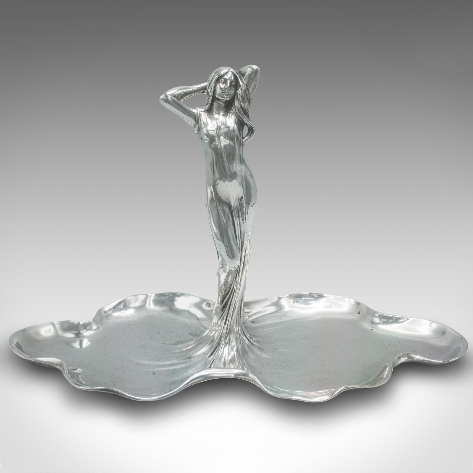 
Se trata de un antiguo centro de mesa Art Nouveau. Bandeja o bombonera decorativa alemana de aleación de fundición, de finales de la época victoriana, hacia 1900.

Cautivadora forma femenina Art Nouveau, de líneas fluidas y magnífica