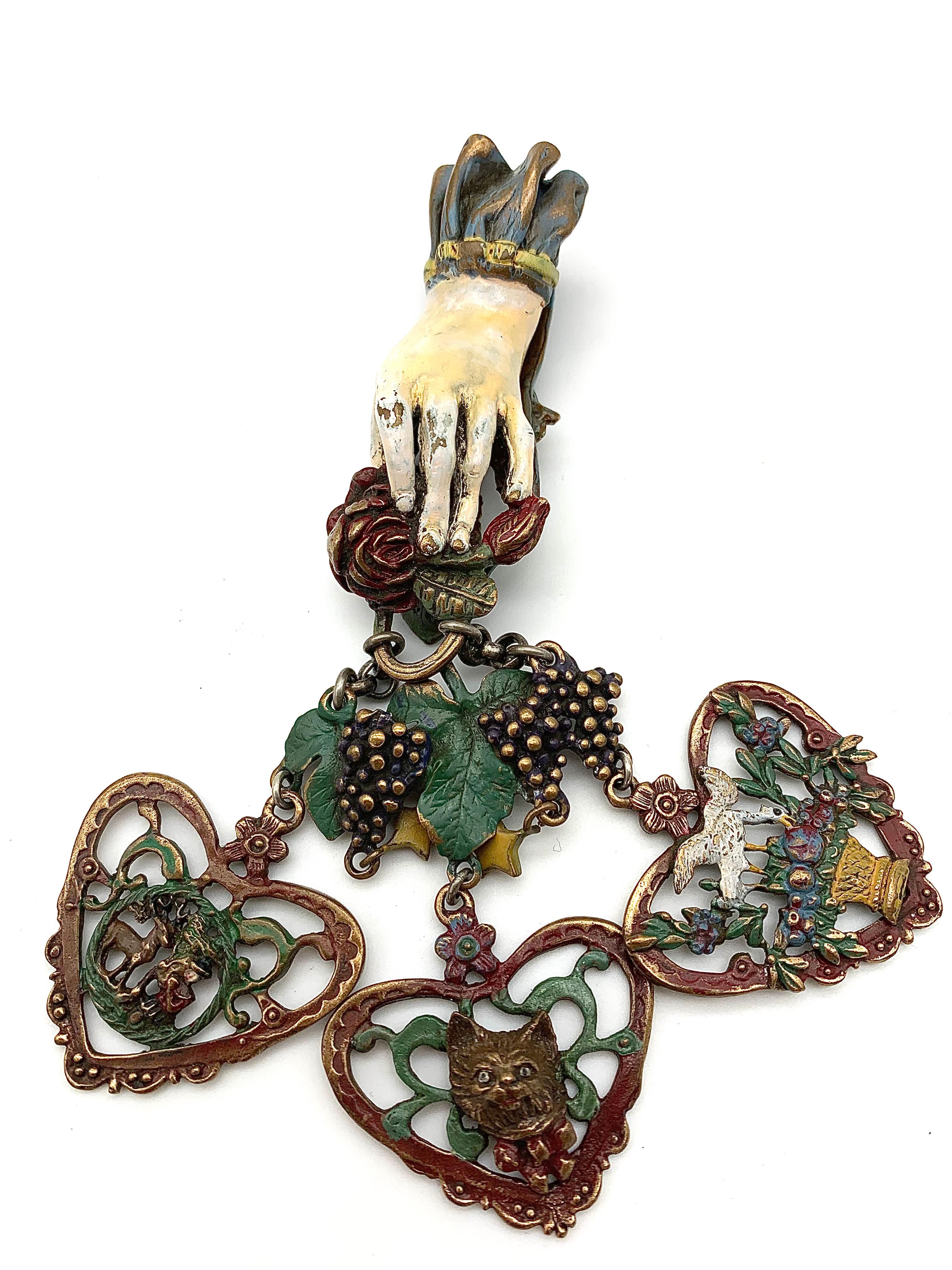 This most extraordinary châtelaine is designed as a delicately modelled hand coming out of a cuff holding a rose and a rose bud. Suspended from the rose are two chains that hold wine leaves and grapes. Attached to the vine leaves and grapes are a