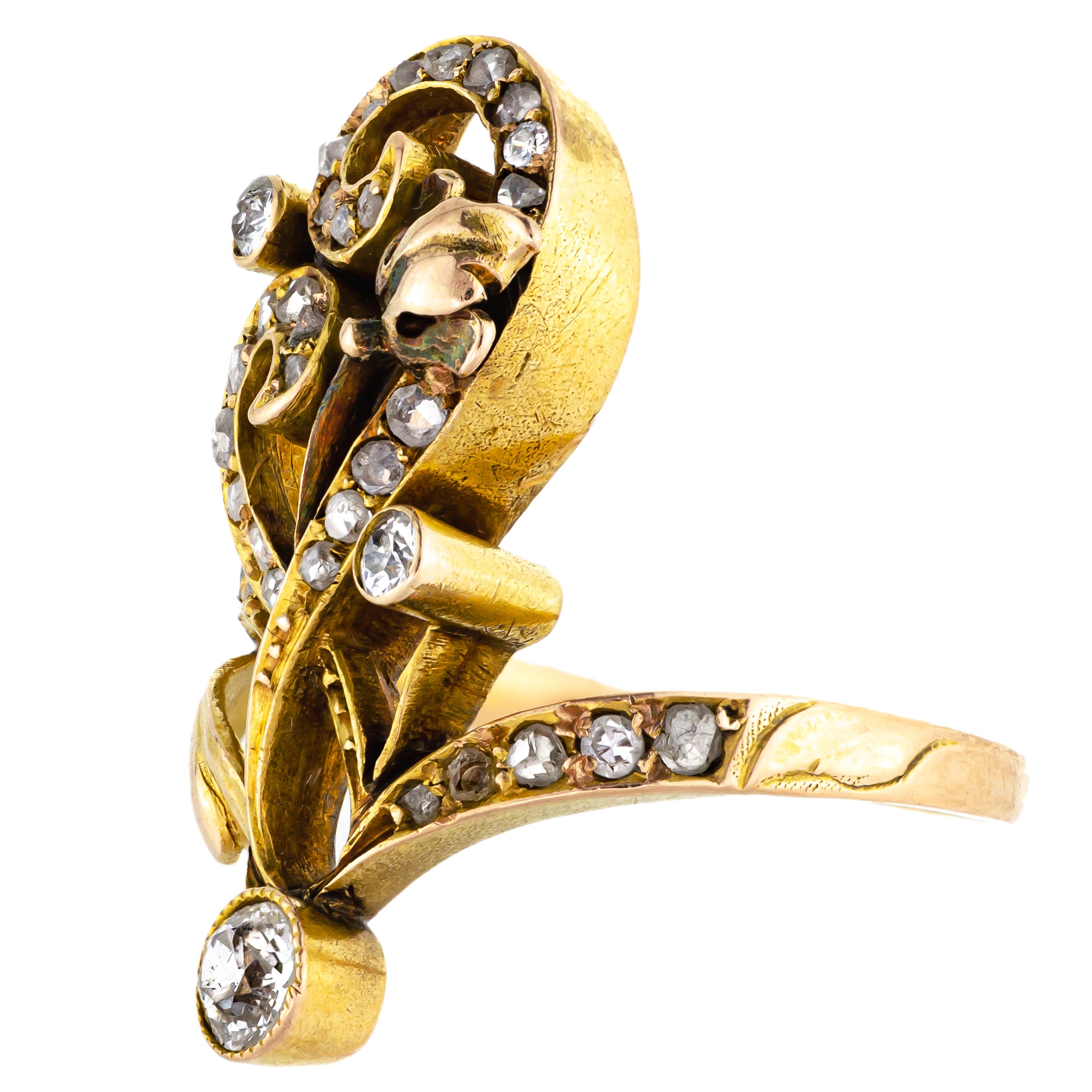 Cette élégante bague longue en or jaune 18kt et diamants Art Nouveau datant de 1900 est un bel exemple de la fluidité du mouvement Art Nouveau. Le motif féminin de la fleur stylisée en forme de tourbillon est réalisé en or jaune 18 carats (testé) et