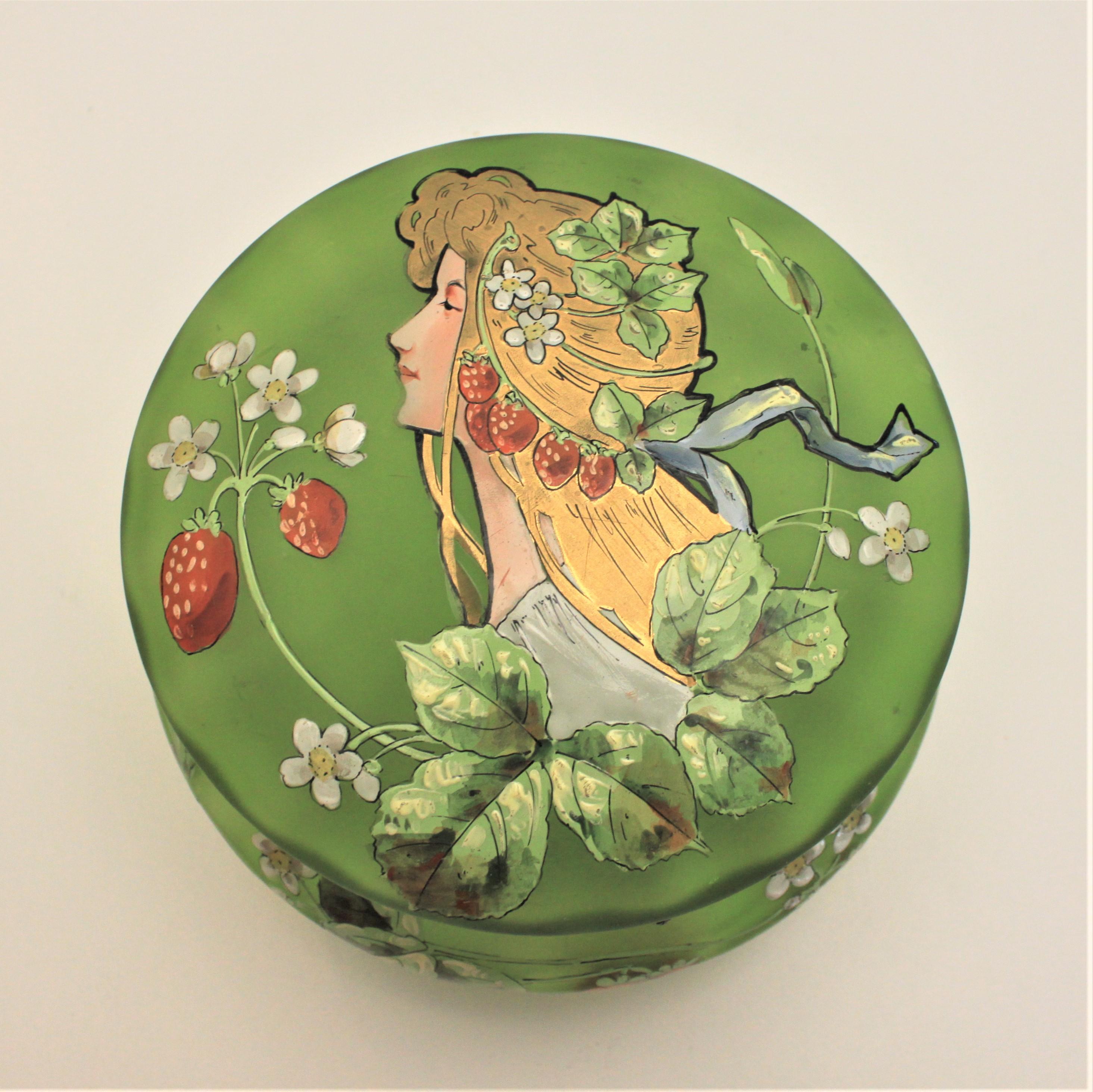 This Art Nouveau enameled green satin glass dresser jar most likely originates from England, but is unsigned. The green satin glass top shows an intricately hand painted portrait of a woman in the Art Nouveau style with strawberries on a flowering