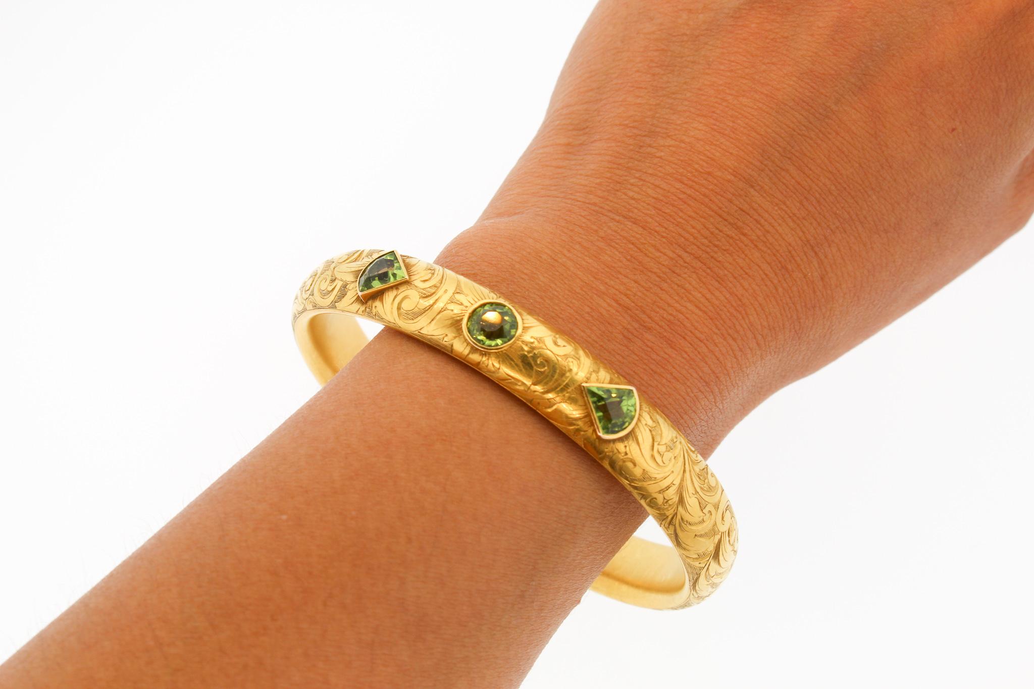 Art Nouveau engraved 14k gold hollow form bangle bracelet set with fancy shaped peridots. The bracelet is extra wide, about 0.40 inches wide, and set with two shield shaped peridot and one round shaped peridot. The bracelet is marked 14k and was