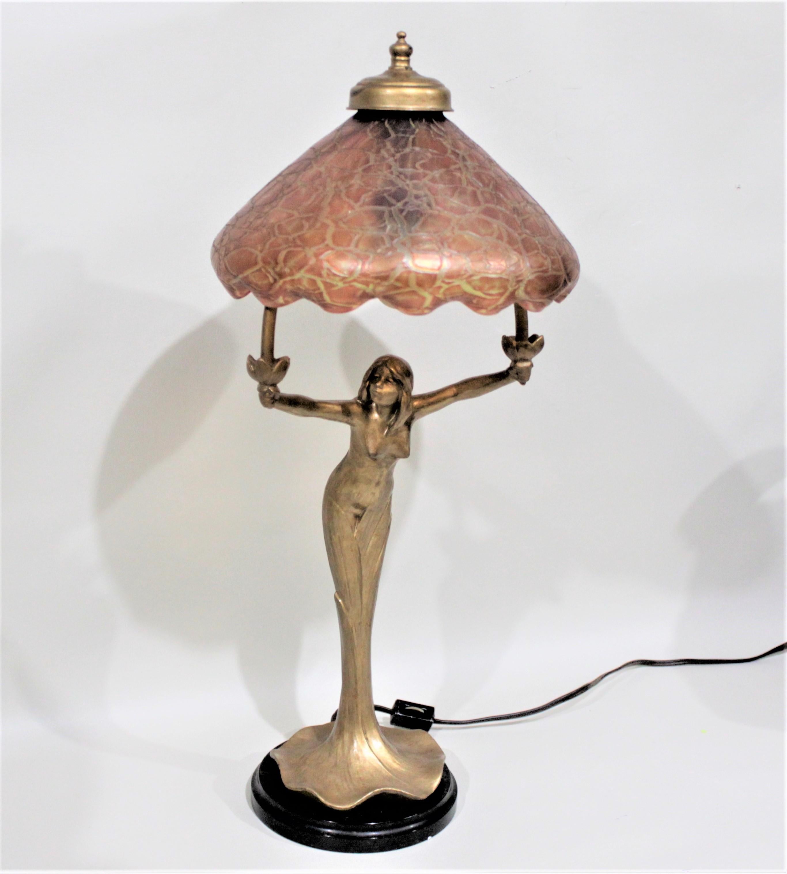 This table lamp is completely unmarked but is presumed to have been made in Europe in approximately 1910 in the Art Nouveau period and style. The figural base of the lamp is a young woman wearing a flowing gown standing with outstretched arms that