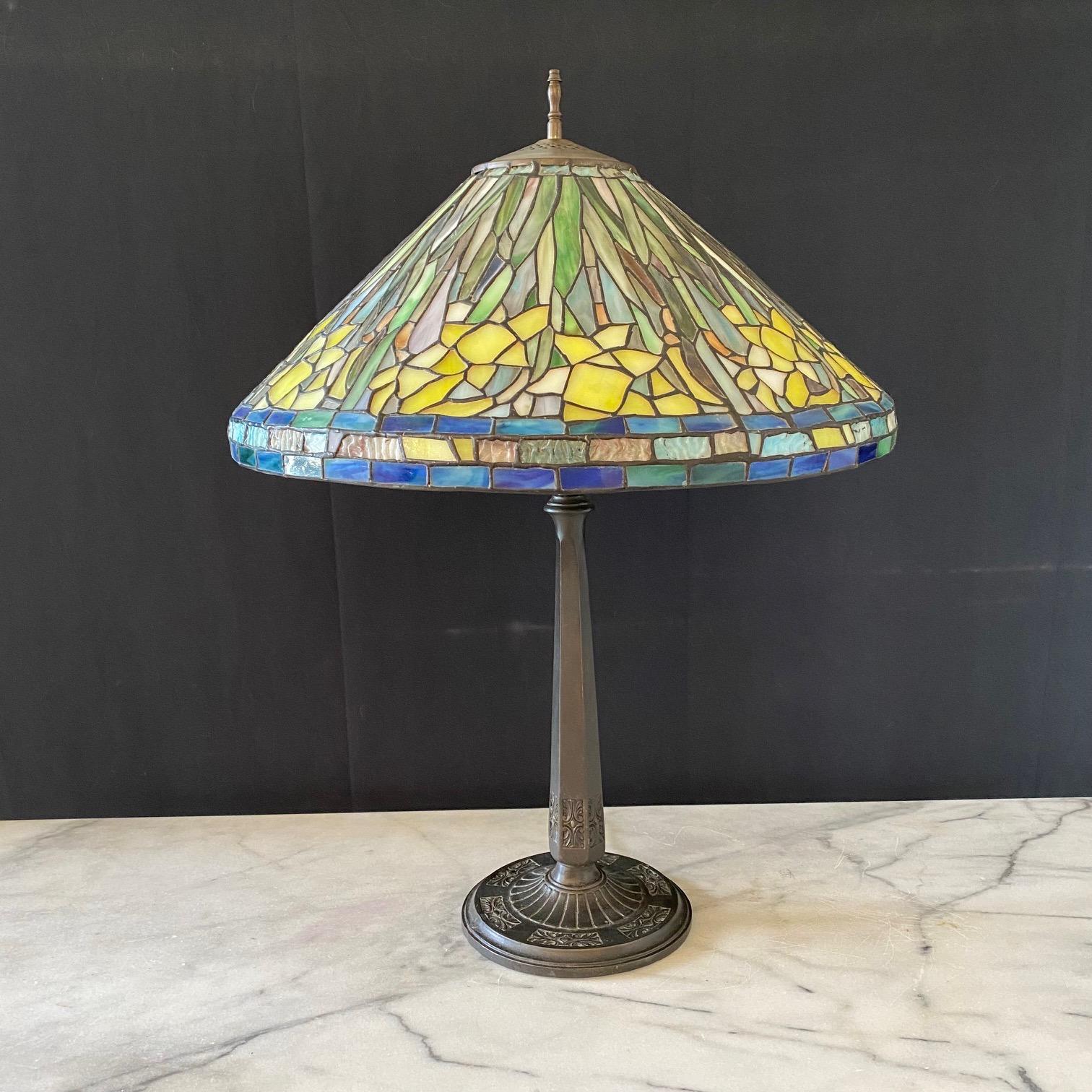  Art Nouveau Tiffany style lamp with multi colored floral patterned glass lampshade typical of the Art Nouveau and Art Deco style having leaded glass pieces in shades of yellow, orange and green with blue trim,  arranged to portray irises in full