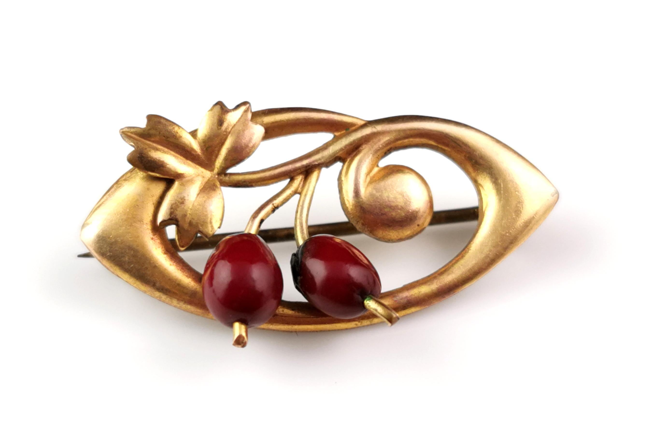 A charming antique Art Nouveau berry brooch.

It is crafted from a rich golden gilt metal and is an ellipse shape with a scrolling leaf design, to the base of the brooch there are two red applied 'berries' made from a rich red early plastic.

The