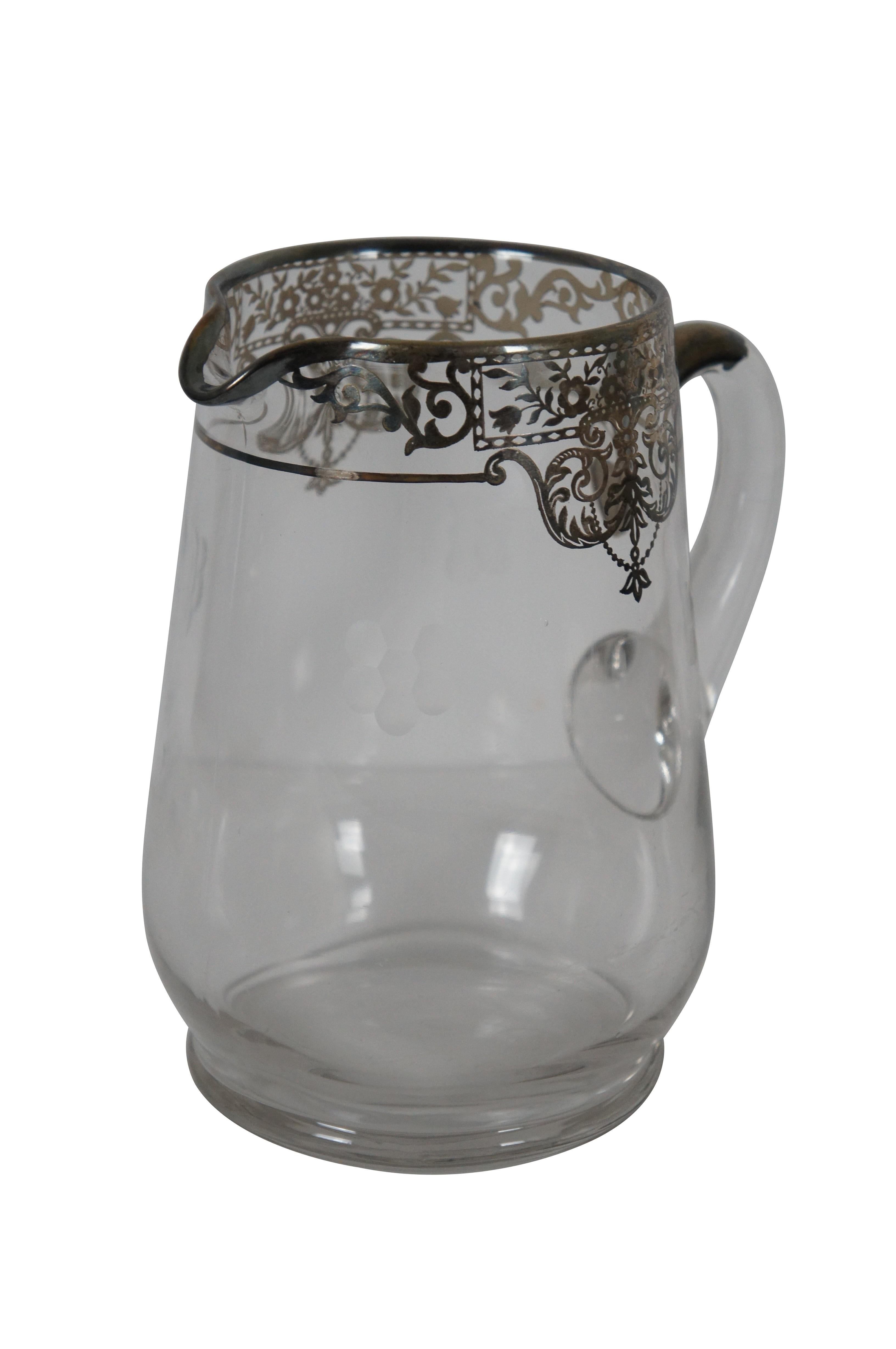 Antique clear glass water pitcher with simple etched flowers and an intricate floral sterling silver swag overlay around the rim and at the top of the handle.

Dimensions:
7” x 5.5” x 7.75” (Width x Depth x Height)