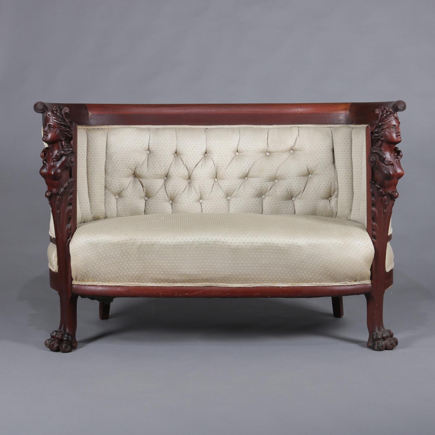 Antique Art Nouveau two-piece parlor set by Karpen features flame mahogany construction in circular canapé form and having arms surmounted in carved figural woman's 3/4 bust and raised on legs with carved paw feet, tuft and button back upholstered