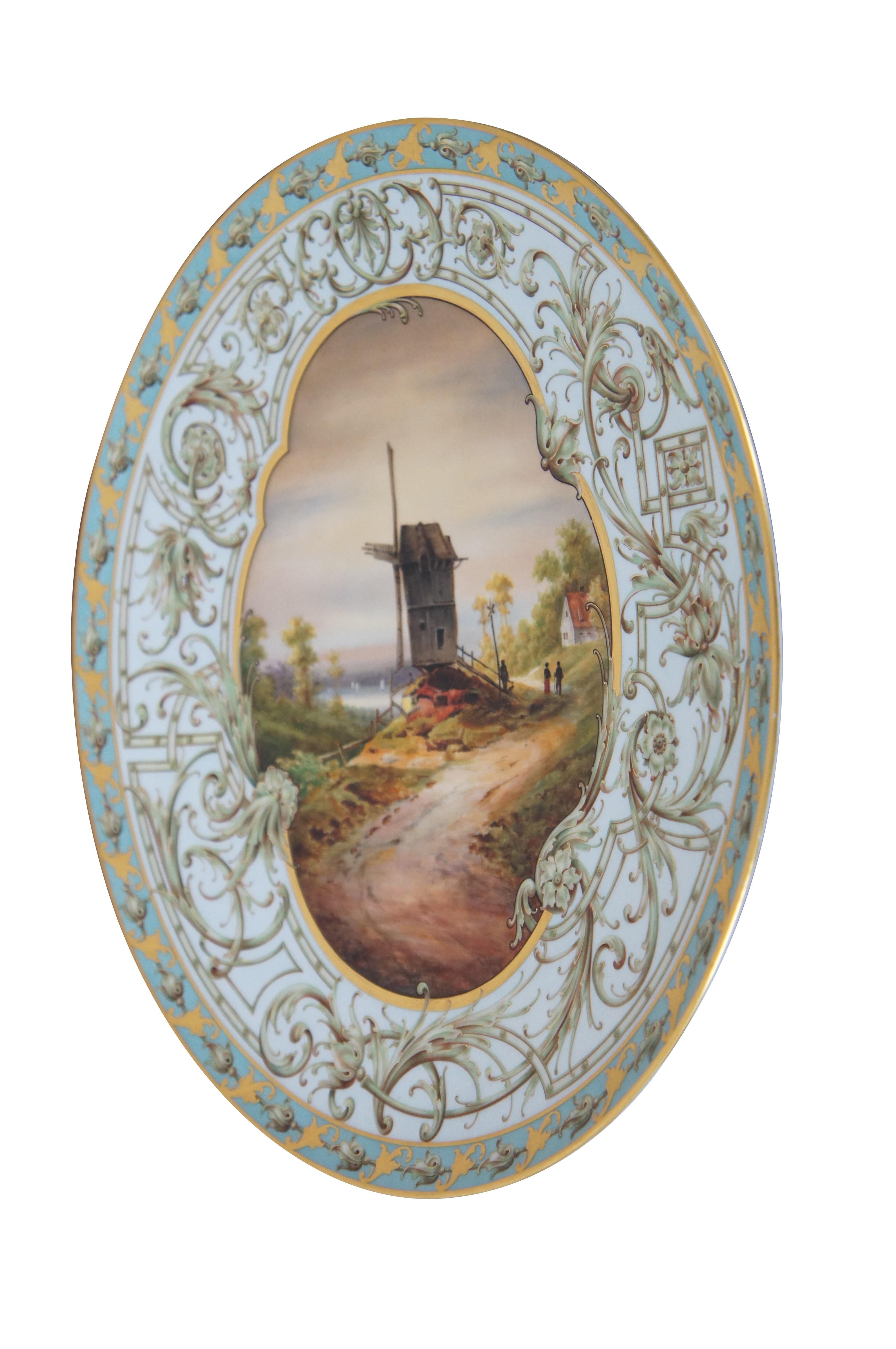Rare antique KPM Berlin porcelain dinner plate, platter or charger featuring central landscape scene that of a windmill, figures, and sailboats surrounded by Art Nouveau design of floral swags / leaves in gold gilt and teal. 

“The Royal Porcelain