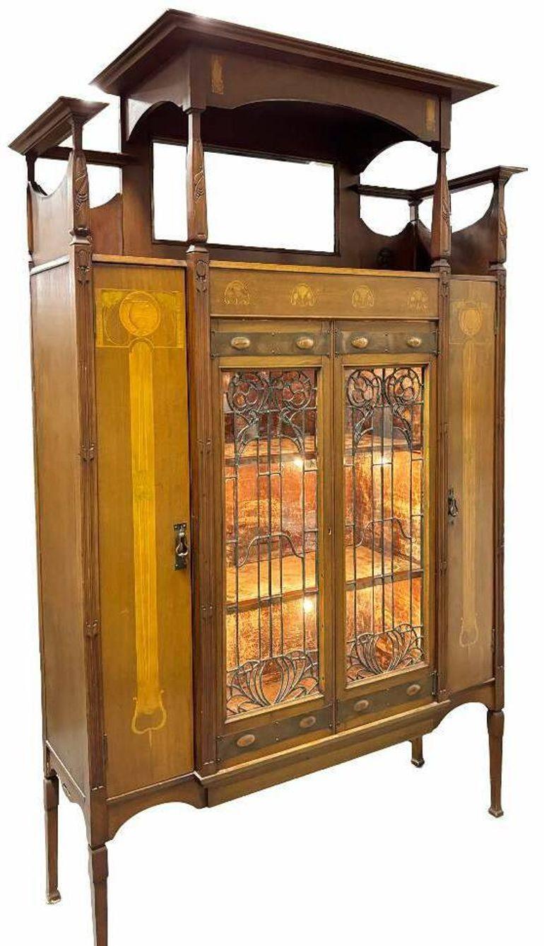 This magnificent Art Nouveau light-up display cabinet showcases exquisite Gallé-style marquetry with floral inlays, likely crafted from sycamore and boxwood in soft golden yellow and chartreuse tones. The carved floral frame and posts complement its