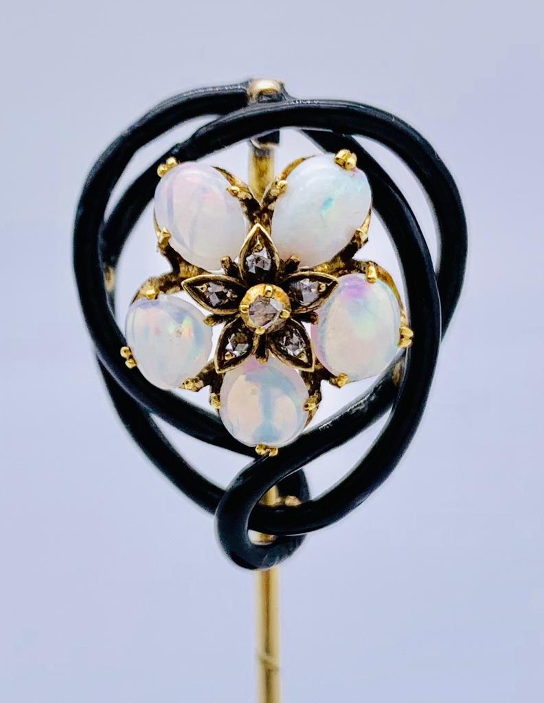 Fünf ovale Opale sind zu einer Blüte angeordnet. Die Blume hat eine sternförmige Mitte, die mit einem größeren und fünf kleineren Diamanten im Altschliff besetzt ist. Opale und Diamanten sind in 14-karätigem Gold gefasst. Die Opalblüte ist von einem