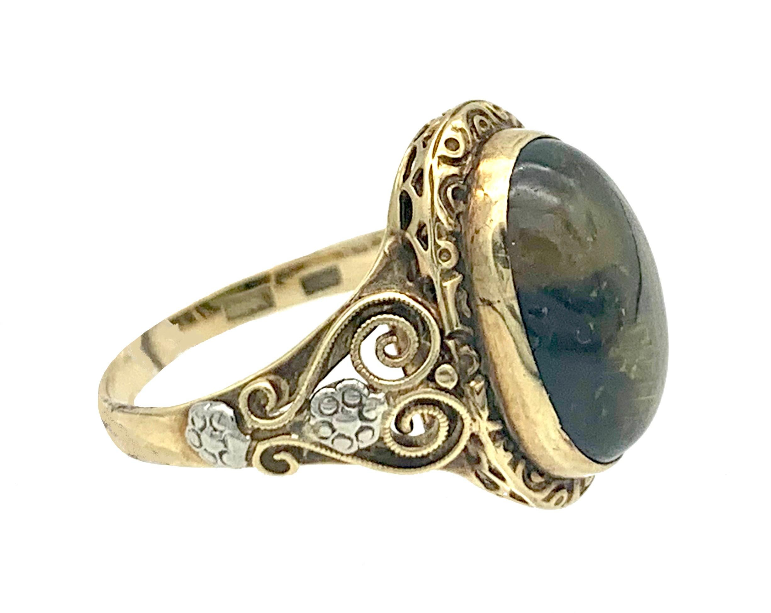This ring was created towards the end of the 19th century out of 14K gold and platinum. This unusual Art Nouveau jewel is set with a green fluorite cabochon in a gold mount within an outer ornamental surround decorated with half bull eyes. The sides