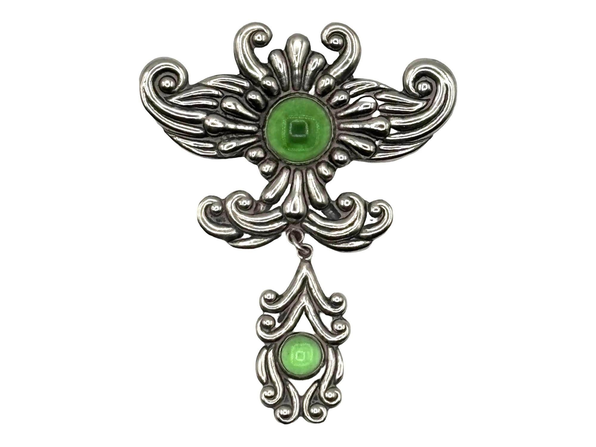 Questa spilla d'argento Art Nouveau d'epoca è caratterizzata da uno splendido centrotavola in stile agata verde, che incarna la bellezza fluida e organica caratteristica dell'epoca. Una delicata lavorazione dell'argento circonda la pietra, form A