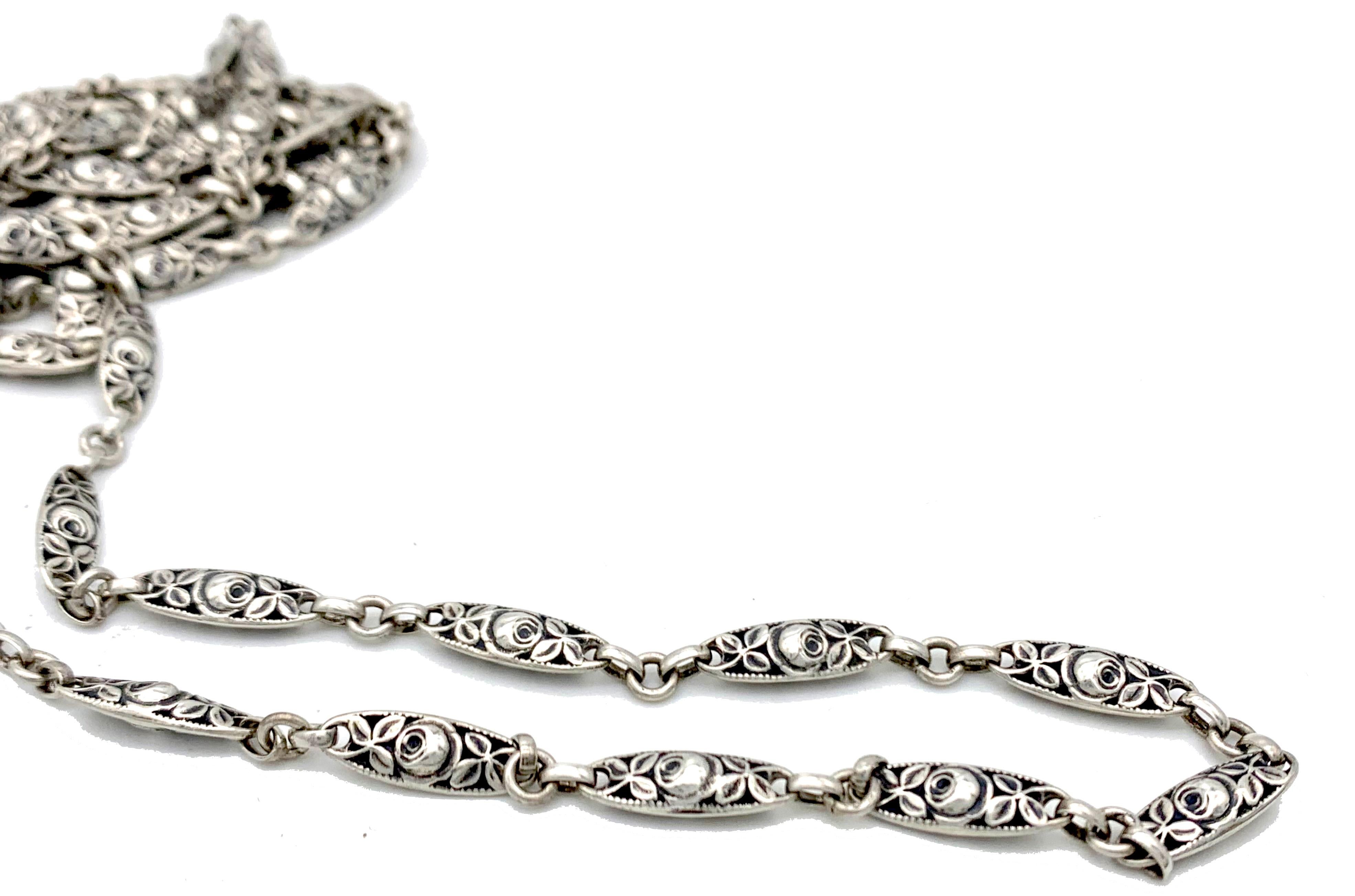 Esta excepcional cadena de guarda larga Art Nouveau de plata está formada por elementos en forma de ojo decorados con rosas y hojas en relieve.