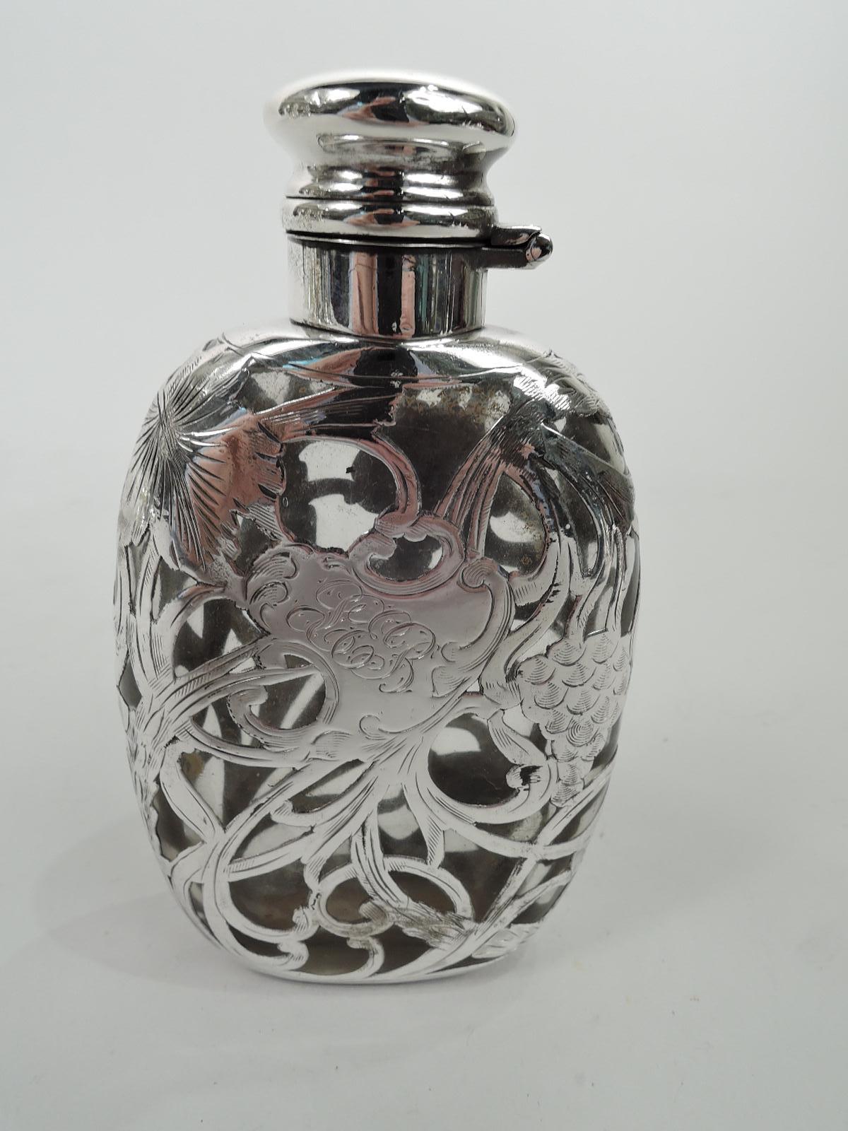 Turn-of-the-century Art Nouveau glass flask with engraved silver overlay. Flat with curved sides. Overlay in form of grain stalks and fruiting grapevine. Asymmetrical cartouche engraved with script monogram. Silver neck collar and hinged and