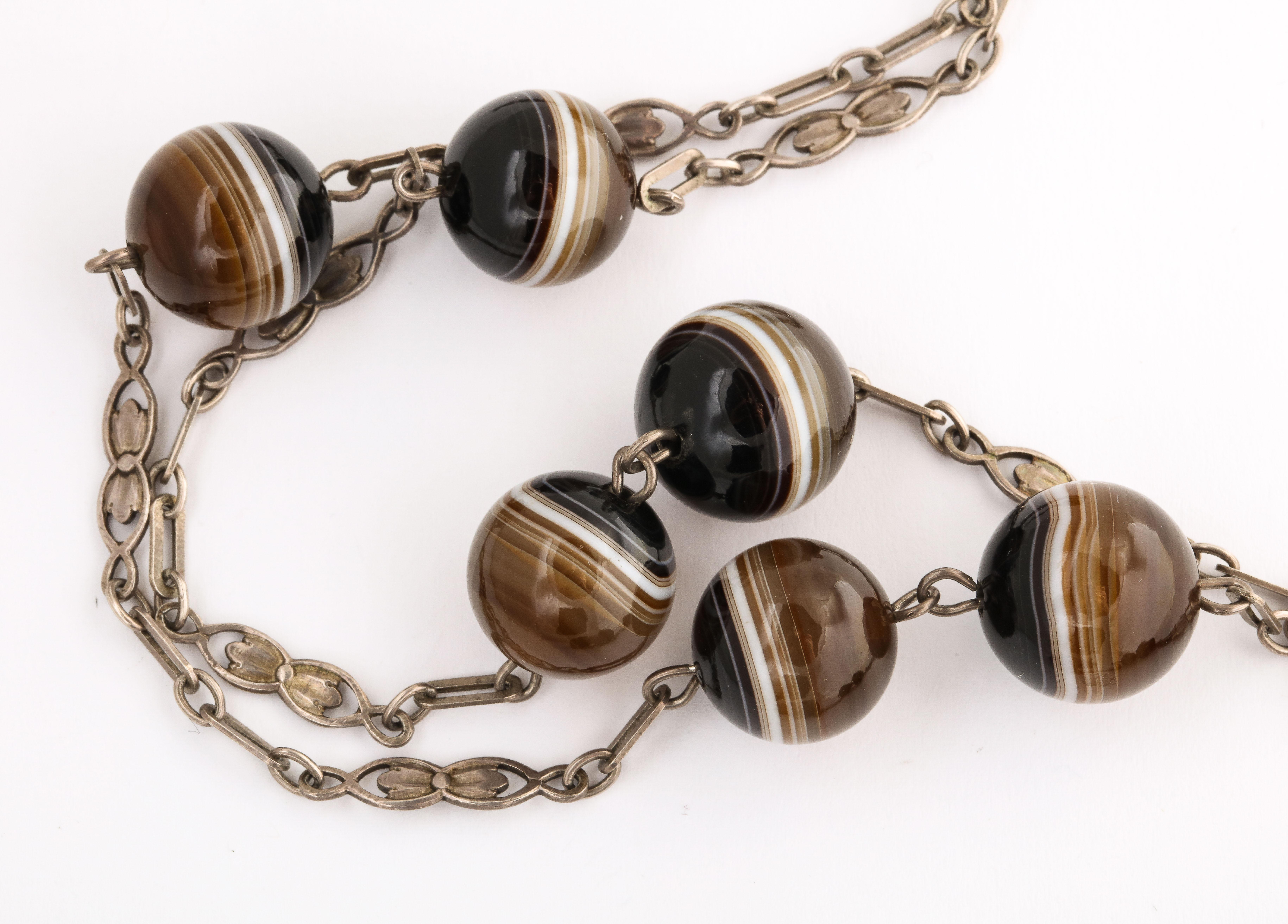 Sturdy alternating links of rectangles and double tulips hold uniform banded agate beads. The distance between the agates vary sometimes kissing cousins sometimes three inches apart and other times five inches apart. The agate balls are brown, white