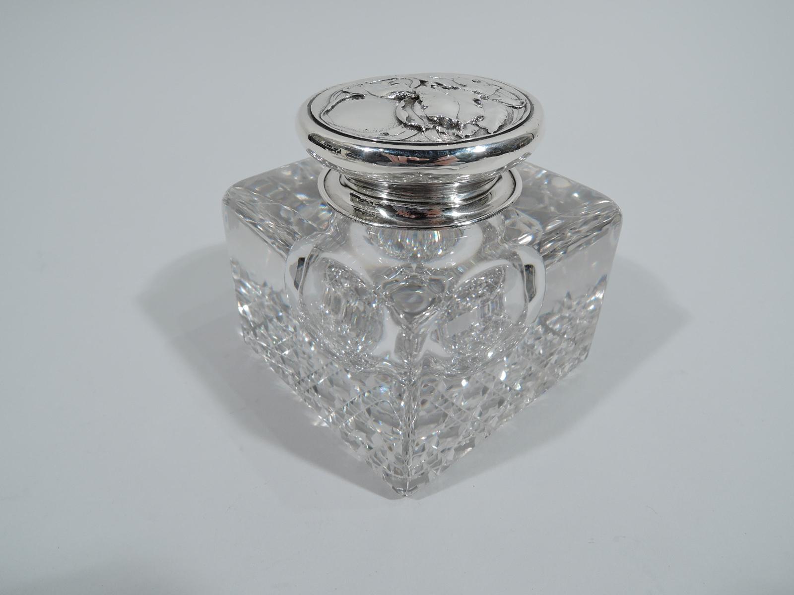 Turn-of-the-century Art Nouveau inkwell. Rectilinear clear-glass block with round well. Diaper cut-to underside. Short neck in sterling silver collar. Cover also sterling silver; top chased with fluid flower heads on stippled ground. Fully marked