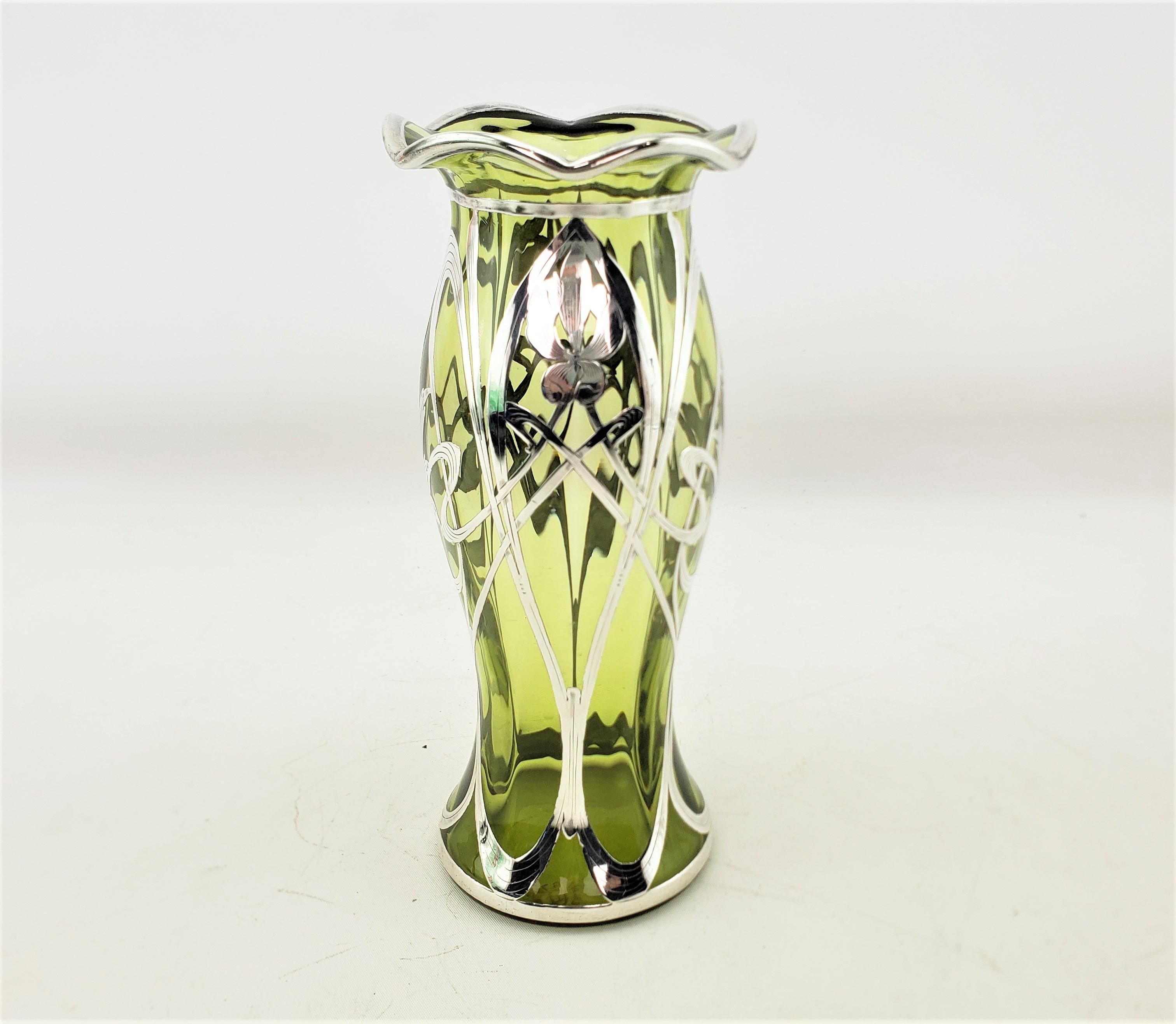 This antique vase is unsigned, but presumed to originate from Austria and date to approximately 1900 and done in the period Art Nouveau style. The vase is composed of a pale green art glass vase with a pie crust edged rim and silver overlay