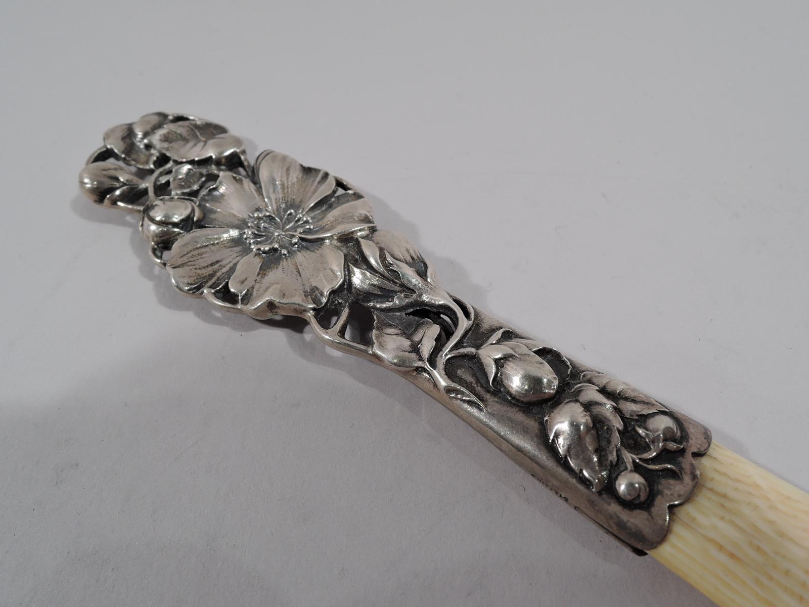 Turn-of-the-century Art Nouveau sterling silver paper knife. double sided sterling silver handle with flower heads and buds entwined and overlapping open scrollwork. Blade flat with pointed tip. Marked “Sterling” and numbered B1830.