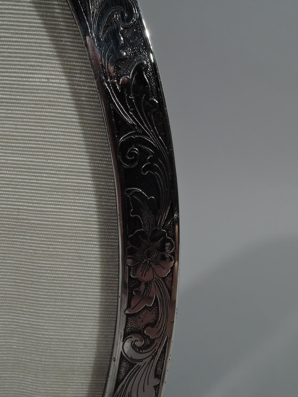 Art Nouveau sterling silver picture frame. Made by Unger Bros in Newark, circa 1910. Narrow oval window and flat surround with acid-etched floral scrollwork on stippled ground. Top and bottom have chevron-shaped cartouches (vacant). Two open bracket