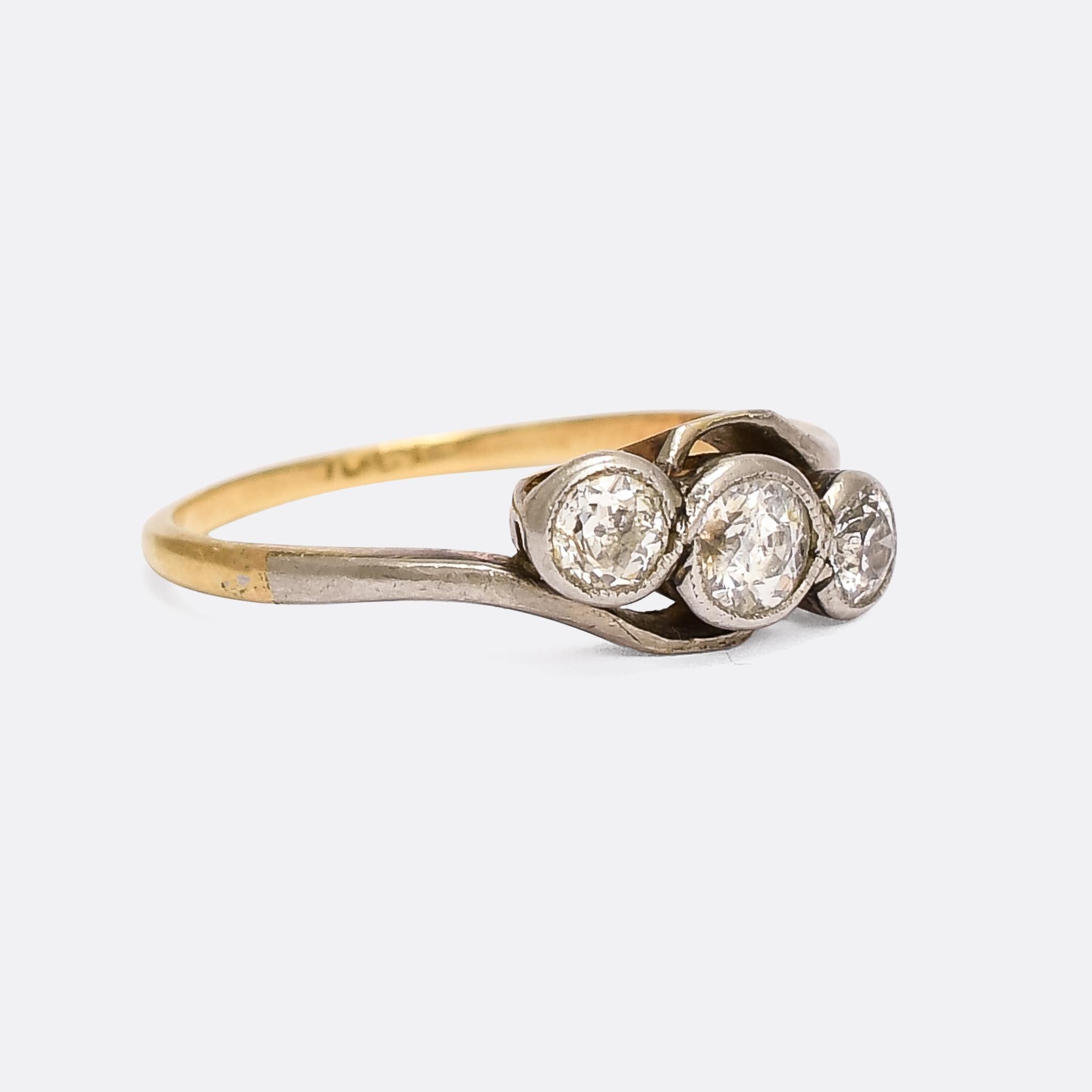 A very pretty turn of the century three stone diamond engagement ring commonly referred to as crossover ring because of the illusion of crossing shoulders. The three sparkling transitional cut diamonds total a little under a carat in weight, and the