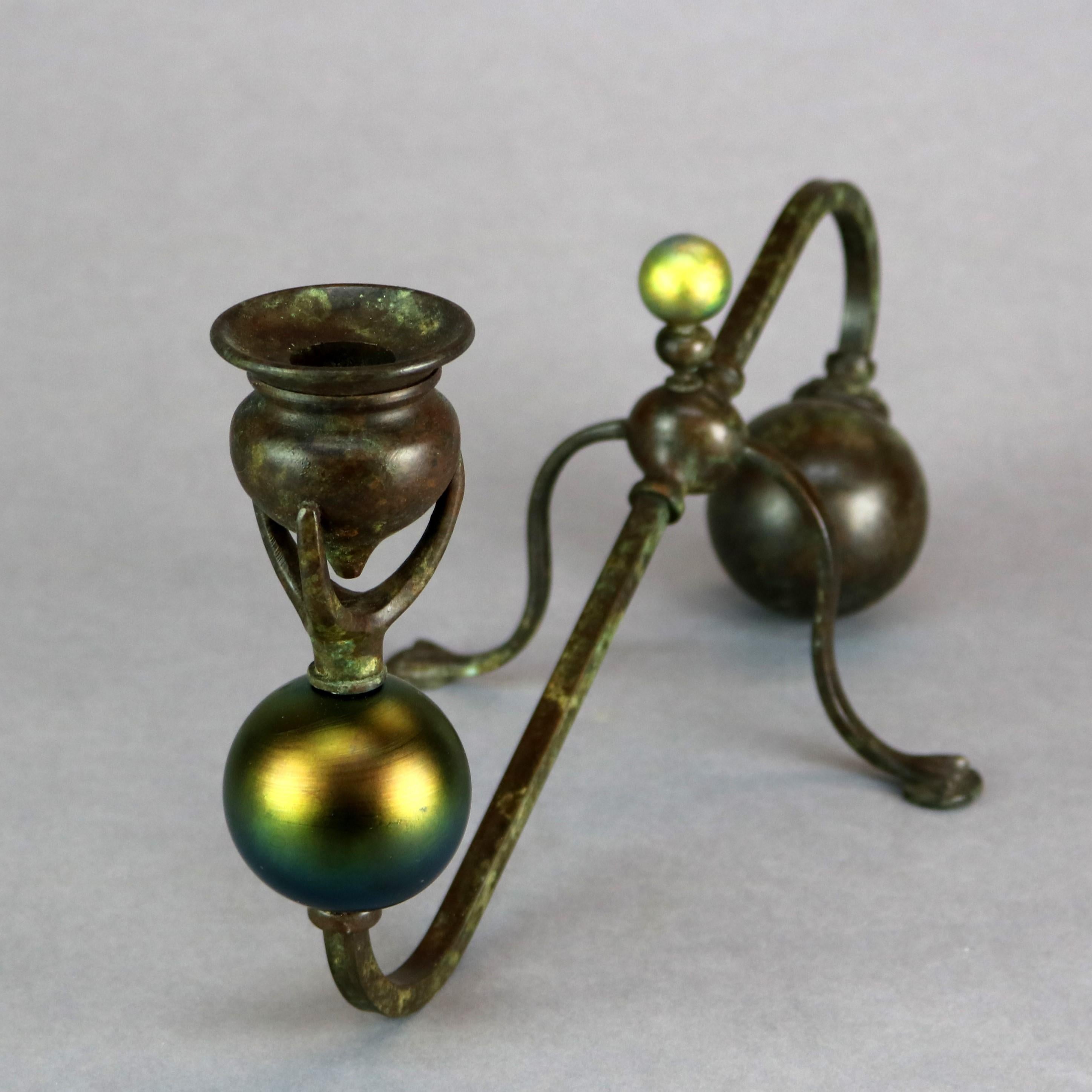 An antique Art Nouveau root candelabra after Tiffany Studios offers bronze frame in organic stylized wave, root or branch form with flanking globes, one bronze and the other art glass and terminating in three prongs cradling an urn form candle