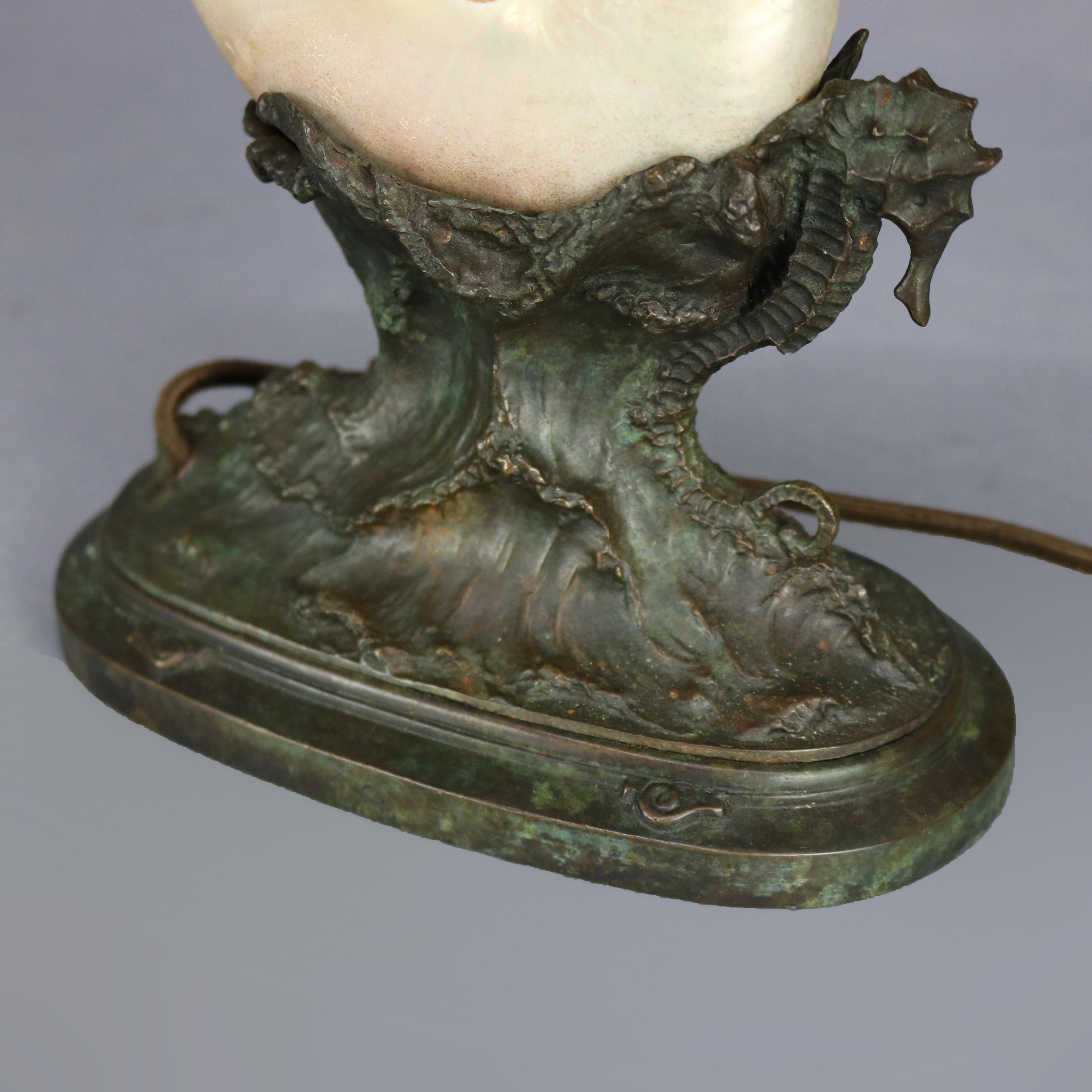 An antique figural ARt Nouveau table or desk lamp by Tiffany Studios offers Nautilus shell shade surmounting cast bronze base with seahorses in the rolling ocean waves, stamped 