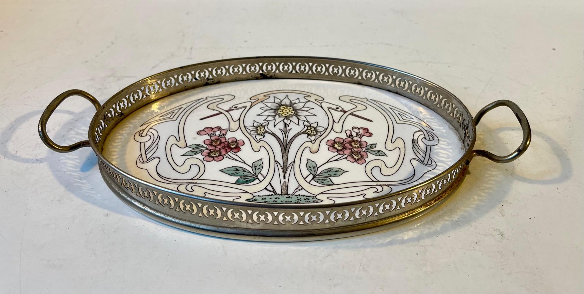 A decorative small sized oval tray in perforated nickel-plated metal and hand painted porcelain. The stars of this motif are two stylized swans that wraps around floral decorations. Stamped decor 1711 and some other numerals to its backside. Unknown