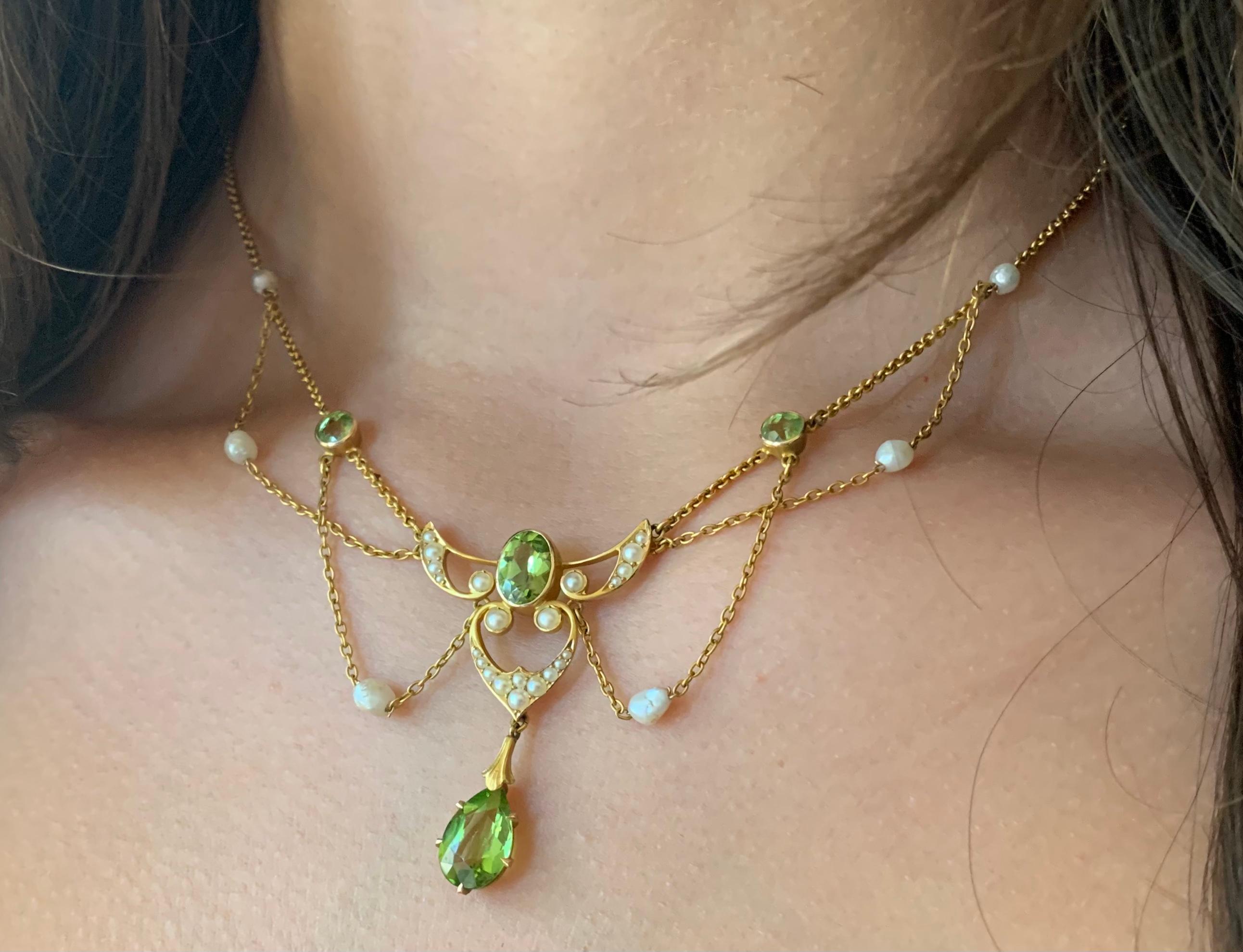 Fine Art Nouveau Edwardian period Winged Heart motif peridot, pearl, 14K yellow gold necklace. 
Circa 1900
The central pearl encrusted heart topped by a pair of pearl encrusted wings with a large 8mm by 5mm oval faceted peridot center, a lovely