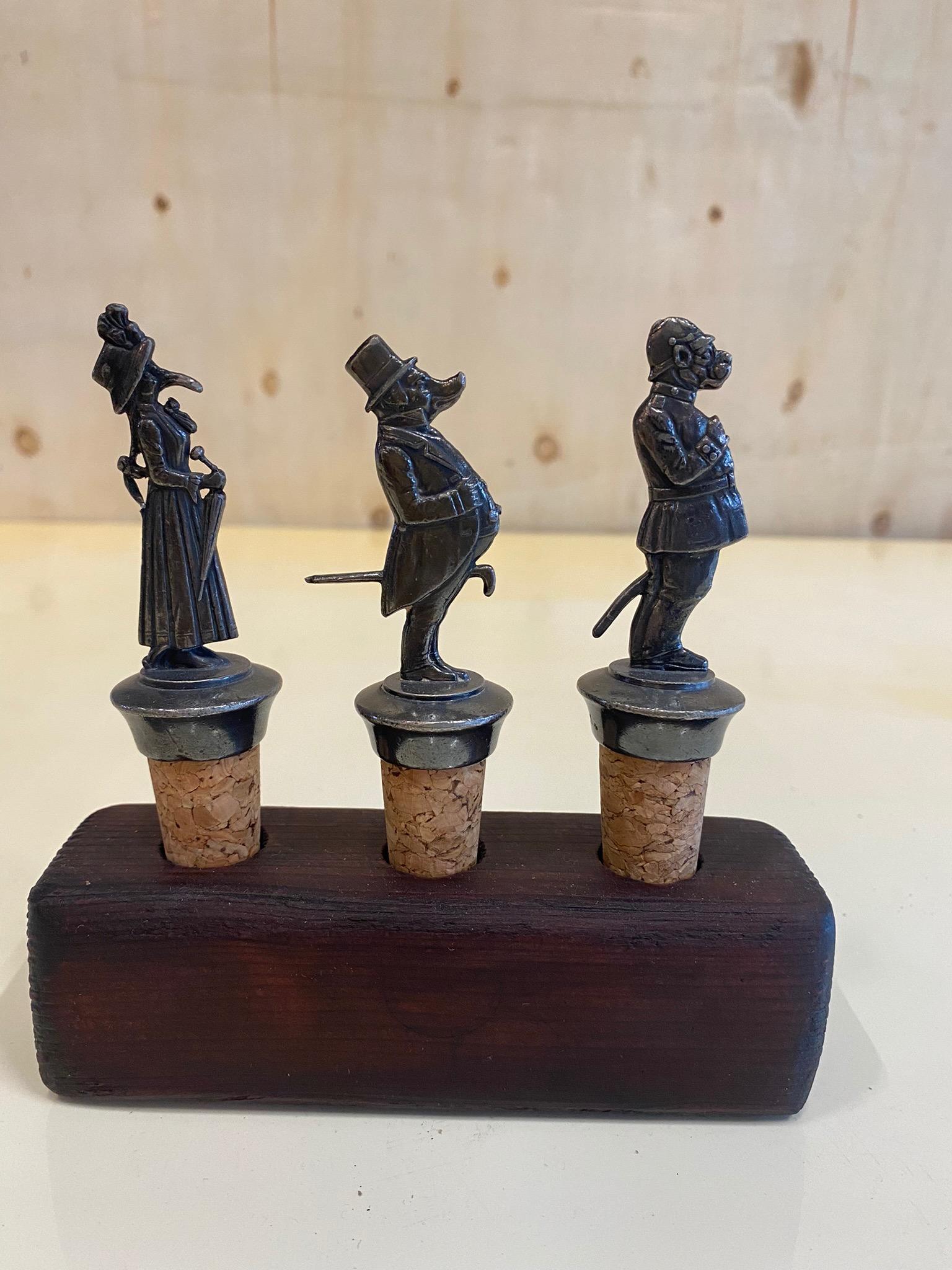 Set of 3 antique art nouveau decorative corks by WMF from around 1910/1920 on a stand made of wood. The 3 bottle caps are made of metal and cork. They are 3 different figures. A bird lady dressed in a swing dress with hat, handbag and umbrella, a