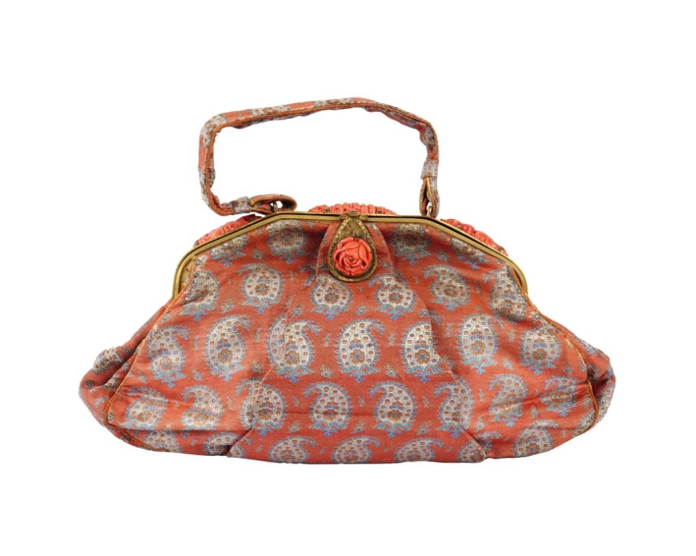 An antique Art Nouveau hand woven textile handbag clutch. Circa the late 19th century. The red bag with a light blue Persian boteh ornament. The brass hardware on the lock and top of the bag are decorated with a sculpted red rose and lush flowers.