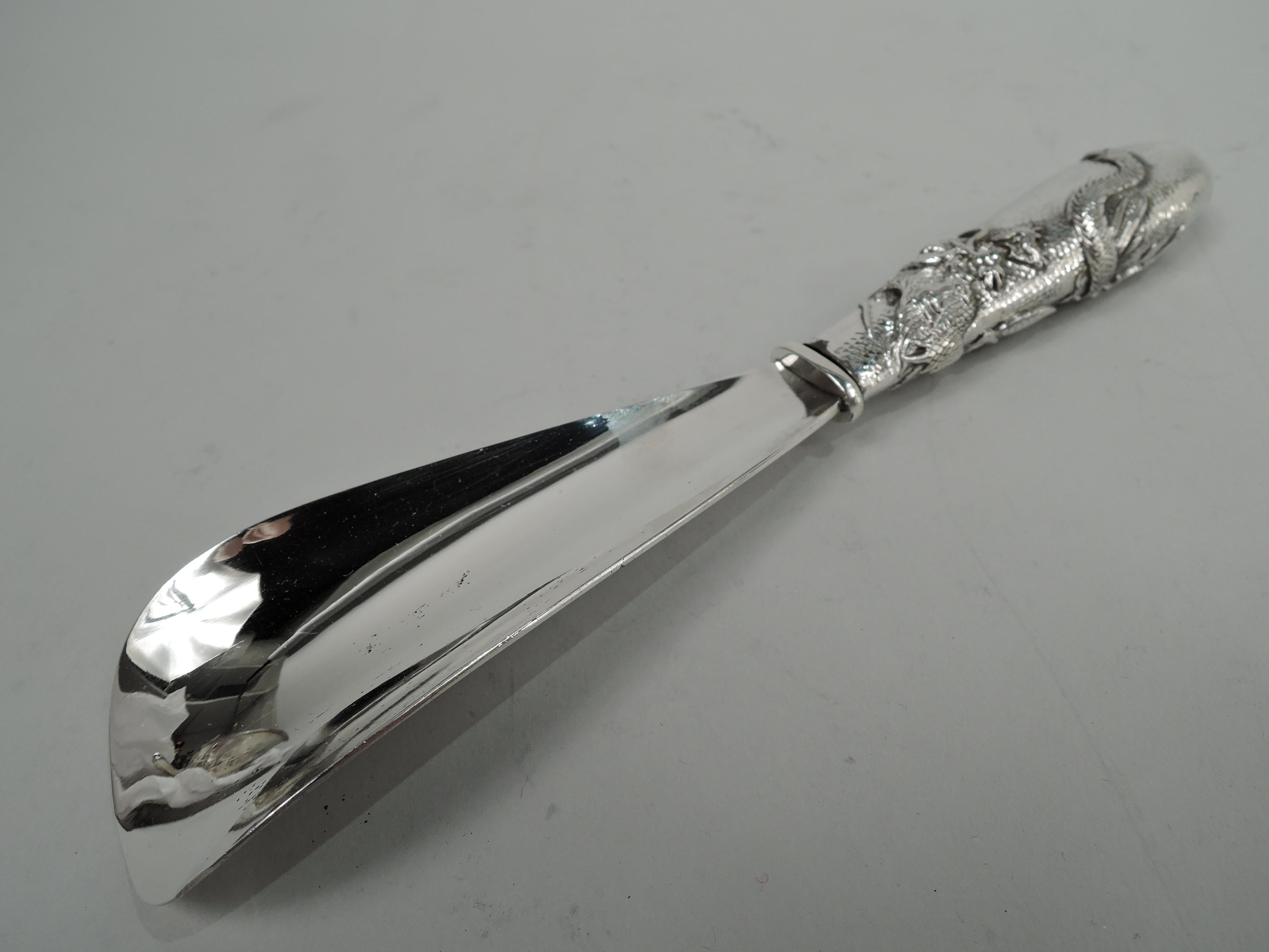 Japanese Meiji silver shoe horn, ca 1900. Retailed by Arthur & Bond in Yokohama. Curved and tapering handle applied with scaly, slithering, horned and taloned dragon; stippled ground. Curved stainless steel blade. Marked “Arthur & Bond / Yokohama /