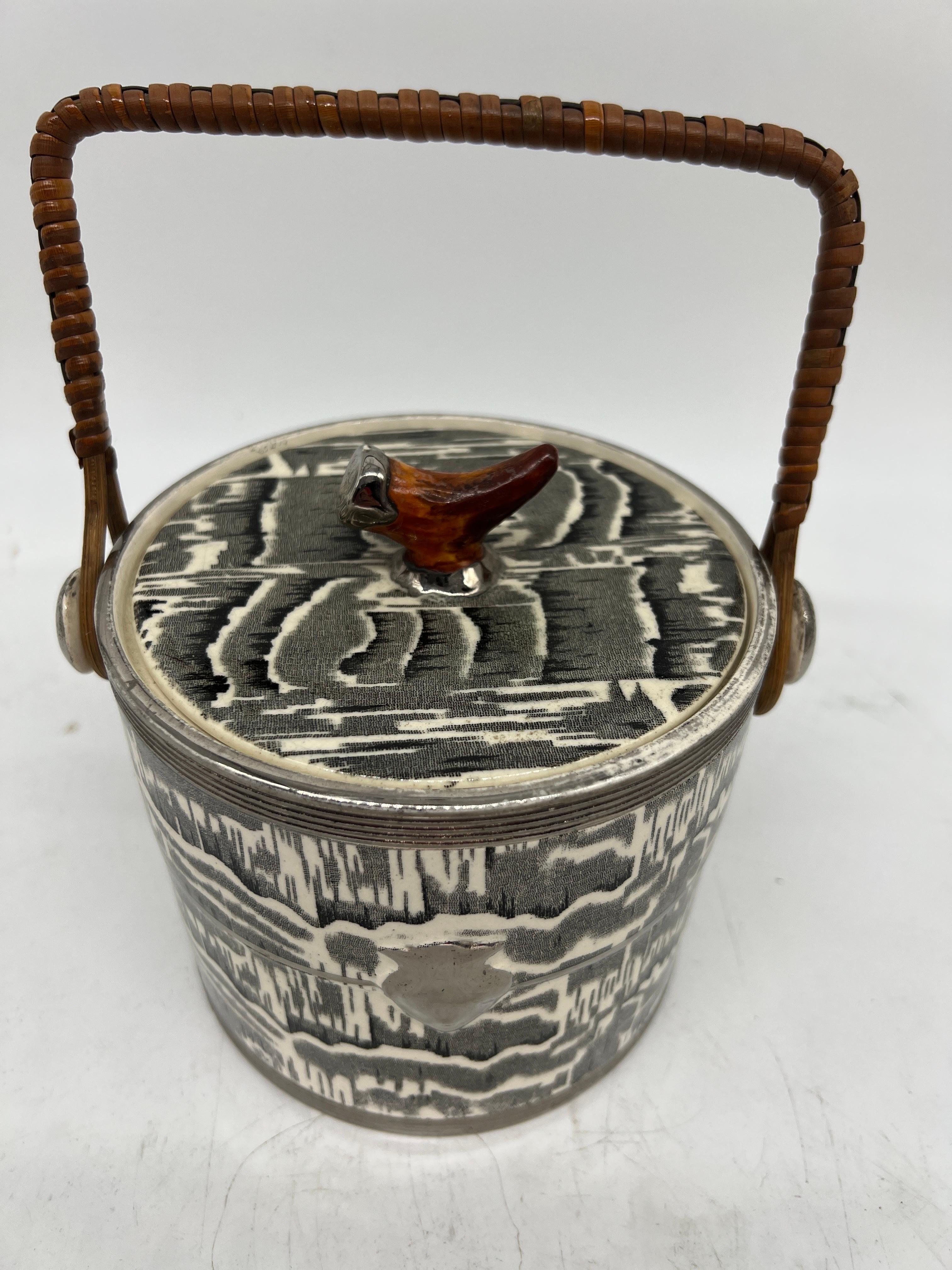 Arthur Wood (English, circa 1930). 

A biscuit barrel made with a ceramic body having faux marbleized surface, wicker handle and a black forest style antler painted finial. Marked to underside appropriately.