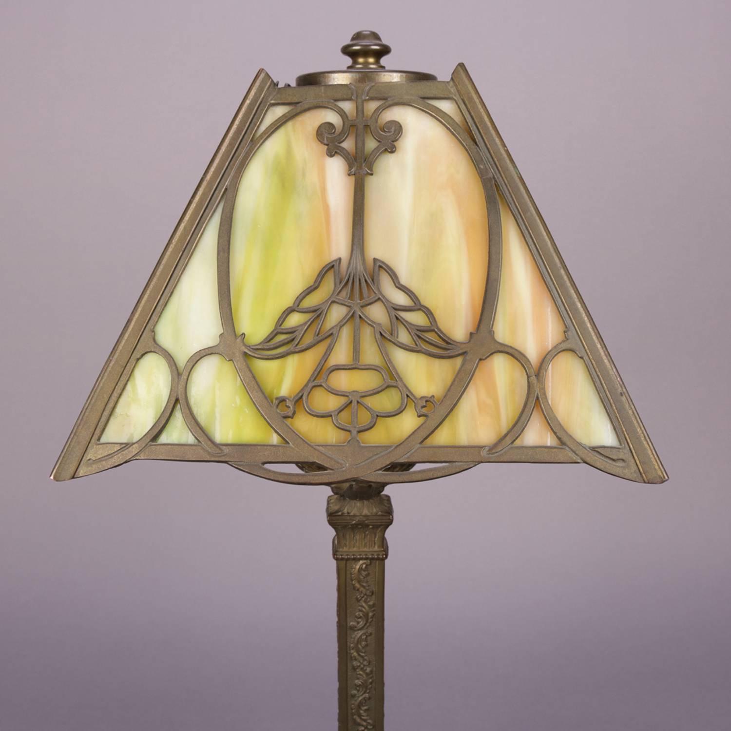 Antique Bradley & Hubbard School table lamp features four panel pierced foliate filigree shade with central stylized flower on each panel and housing slag glass panes, cast base is footed and with embossed foliate decoration, circa