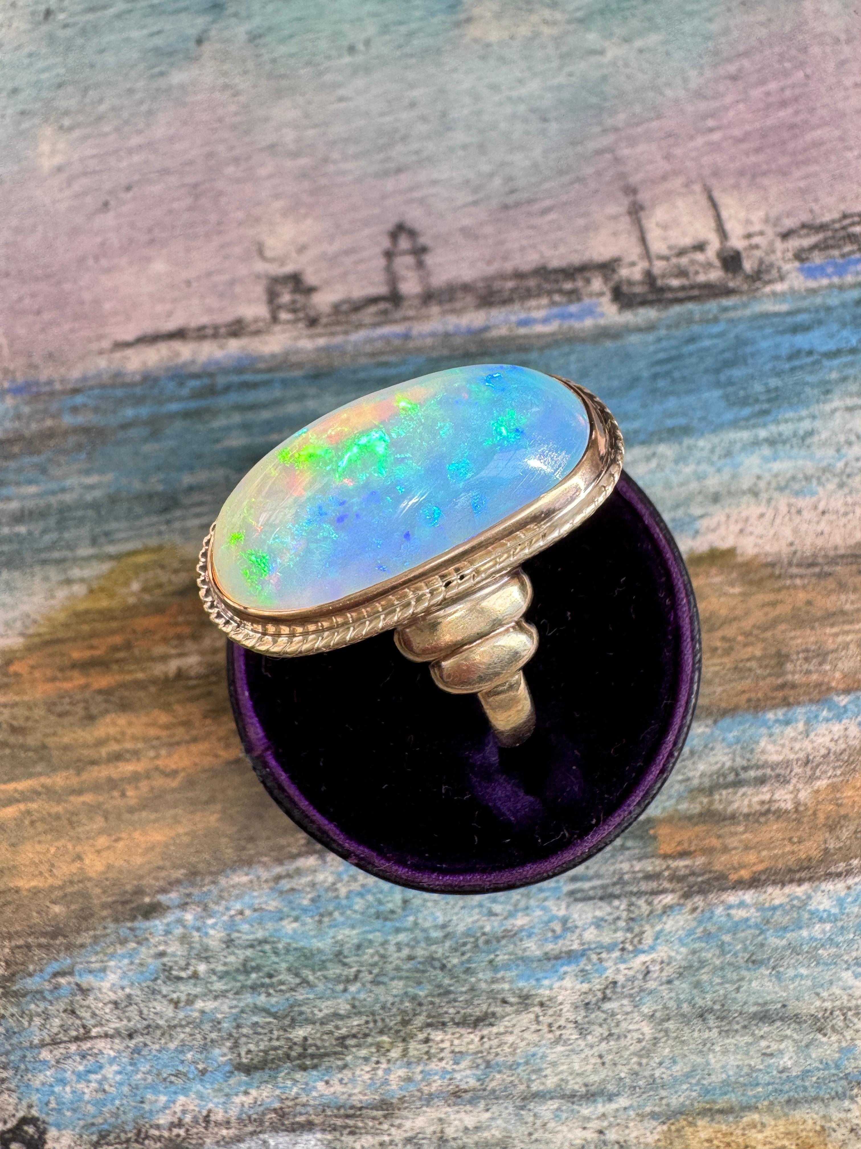 Con una misura di poco inferiore a 1 pollice, questo incantevole anello dell'epoca Arts and Crafts mette in mostra un opale da 9,6 carati con un'ipnotizzante visualizzazione di macchie color arcobaleno. L'opale è incastonato in un castone d'oro rosa