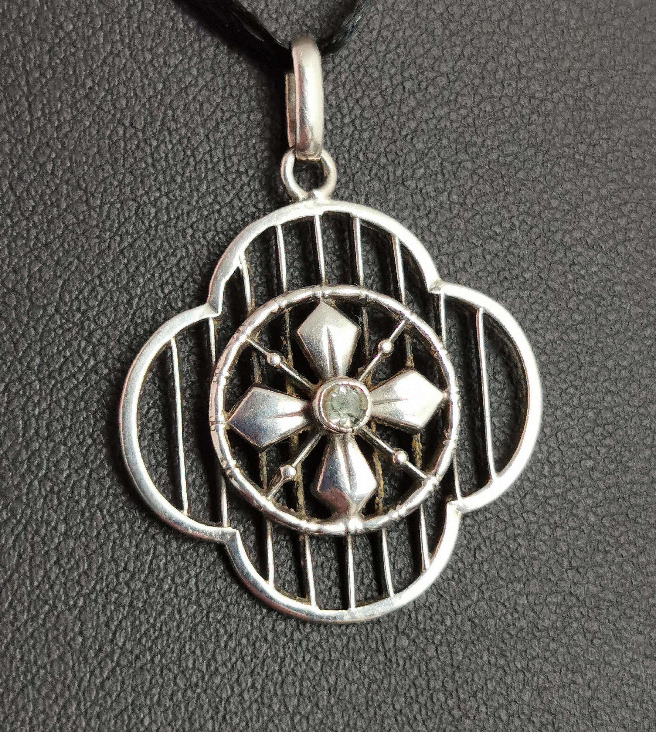 A beautiful little Arts and Crafts era silver and paste pendant.

It is crafted in sterling silver and set with a single clear paste stone.

The pendant has a pretty openwork design with a Quatrefoil shape, geometric vertical lines and a central