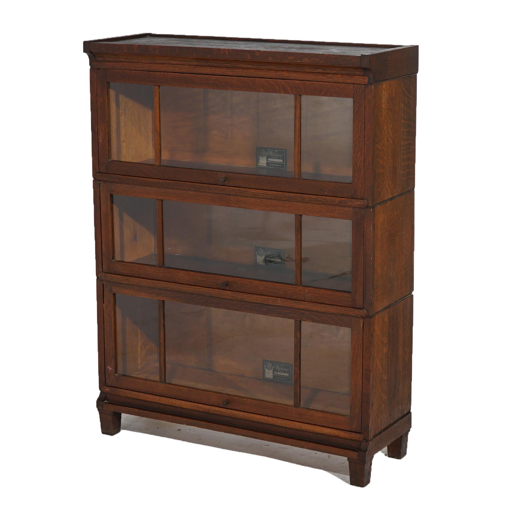 An antique Arts and Crafts barrister bookcase by Viking offers quarter sawn oak construction with three stacks, each having pullout glass doors, raised on square and slightly tapered legs, maker labels as photographed, c1910

Measures - 45
