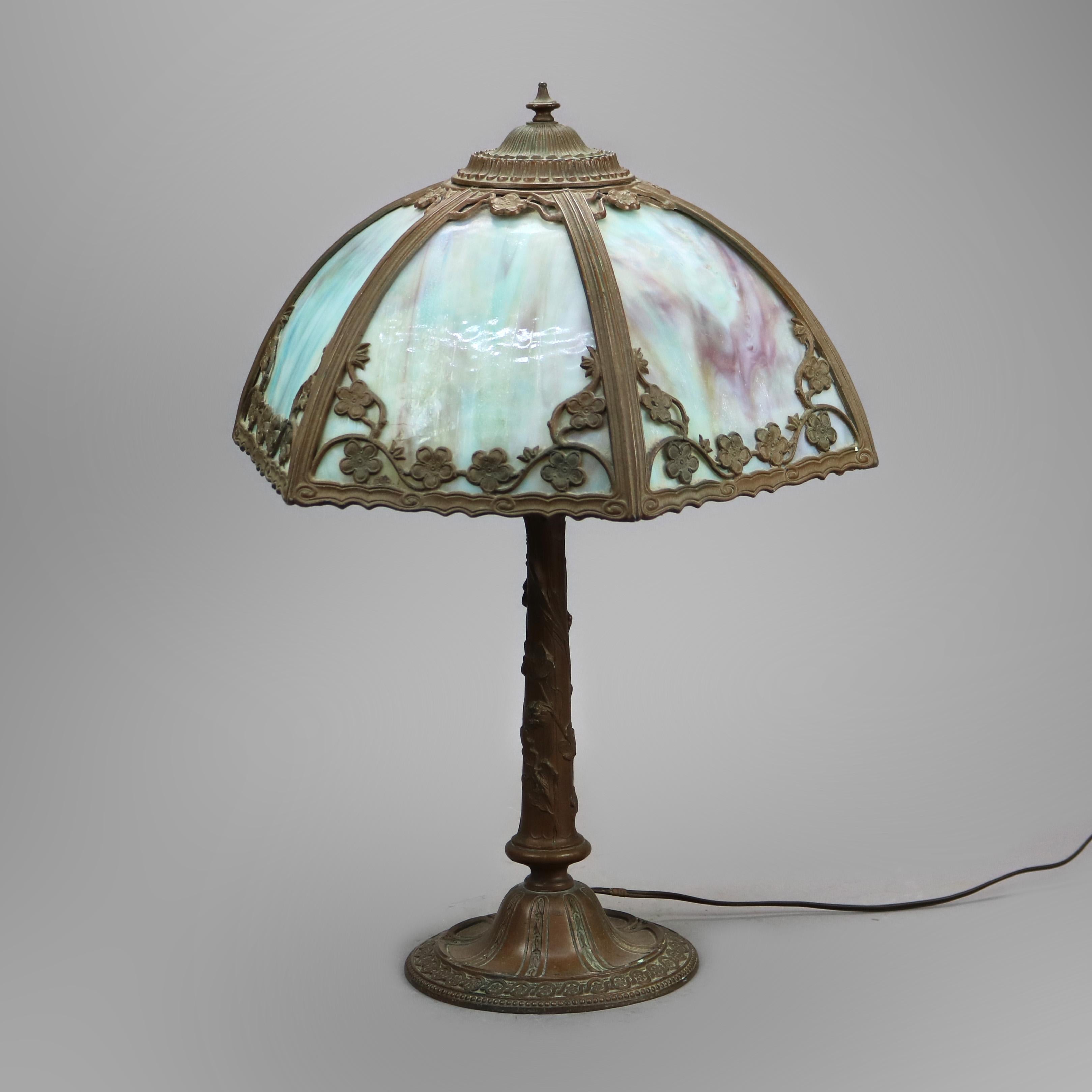An antique Arts & Crafts table lamp in the manner of Bradley and Hubbard offers cast foliate filigree shade housing bent slag glass panels over single socket cast base, maker mark on base as photographed, c1920

Measures - 22.5'' H x 14.75'' W x