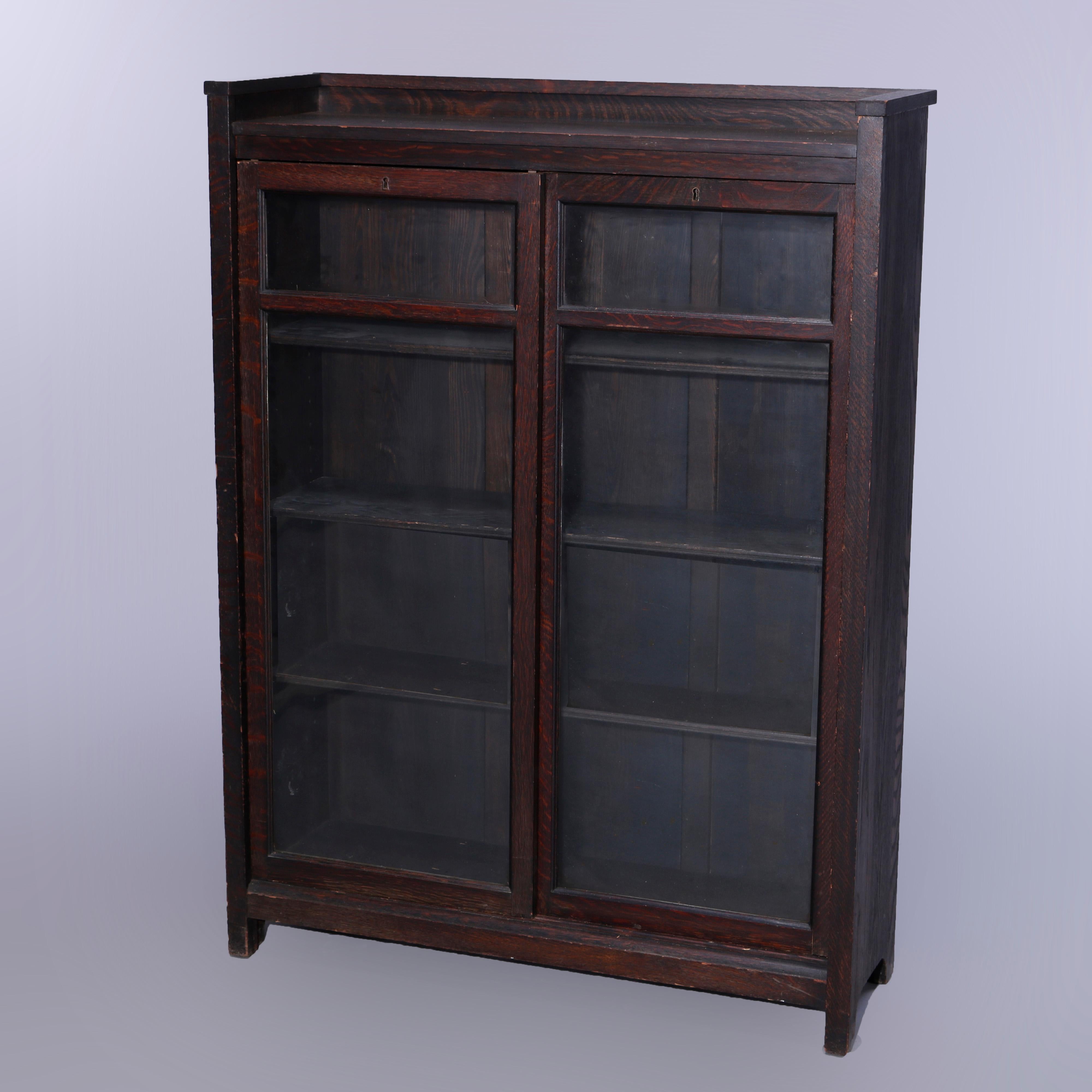 An antique Arts and Crafts Mission enclosed bookcase offers quarter sawn oak construction with upper gallery surmounting case with sliding glass doors opening to shelved interior, raised on square and straight legs, c1910

Measures - 53.75''H x