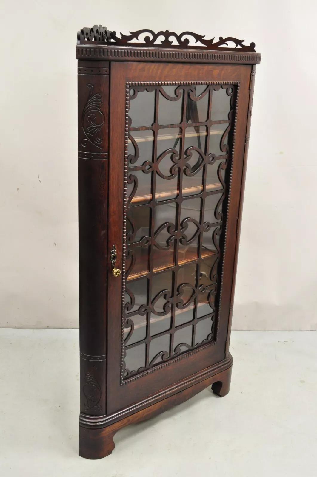 Antique Arts & Craft Oak Wood Glass One Door Fretwork Corner China Cabinet Curio. Item features four adjustable wooden shelves, single large swing door with carved fretwork, unique corner form, working lock and key. Circa Late 19th Century.
