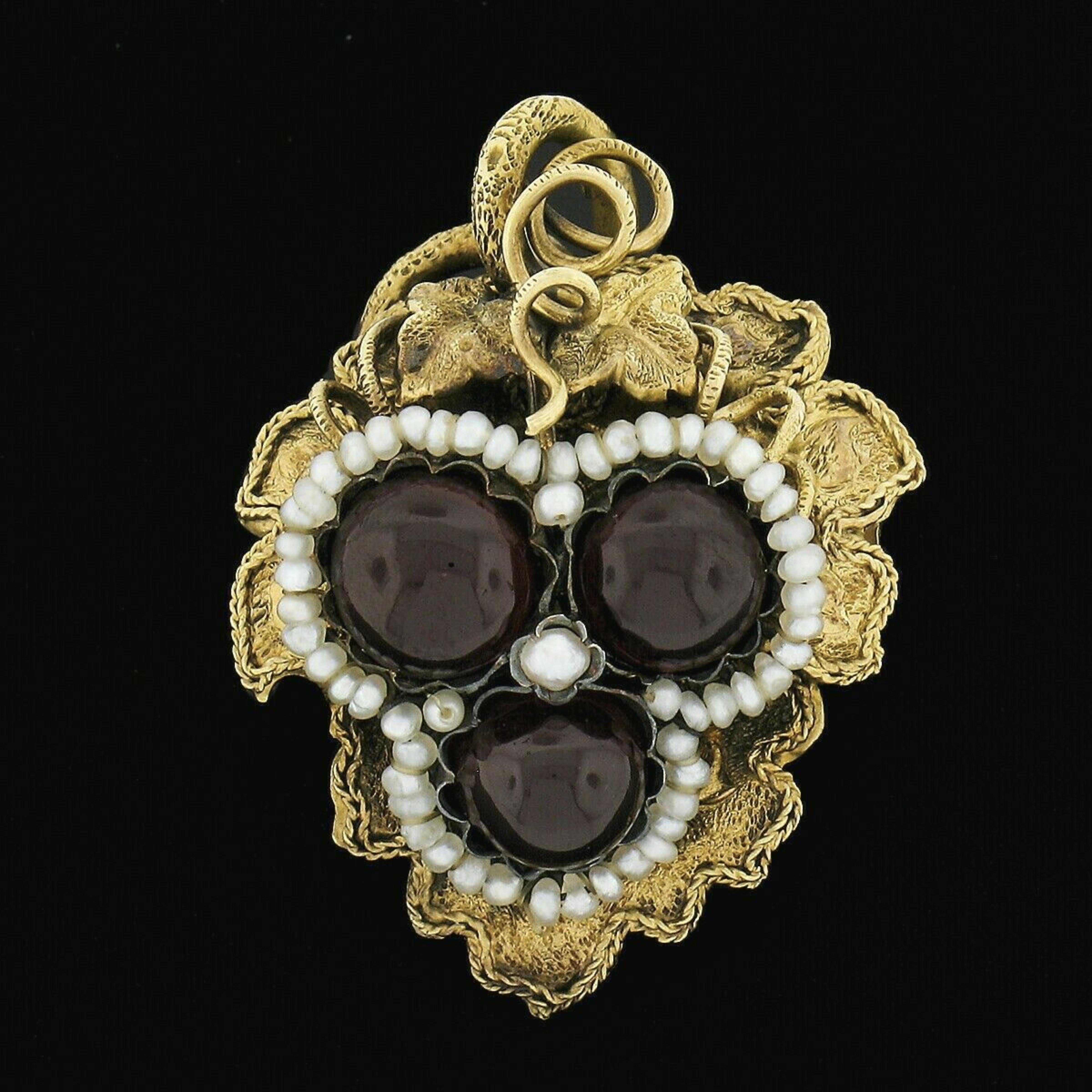 This elegant antique brooch or pendant is crafted in solid 14k yellow gold and features a beautifully detailed 3D foliage design set with a cluster of fine garnets and seed pearls at its center. The three natural garnets are round cabochon cut and