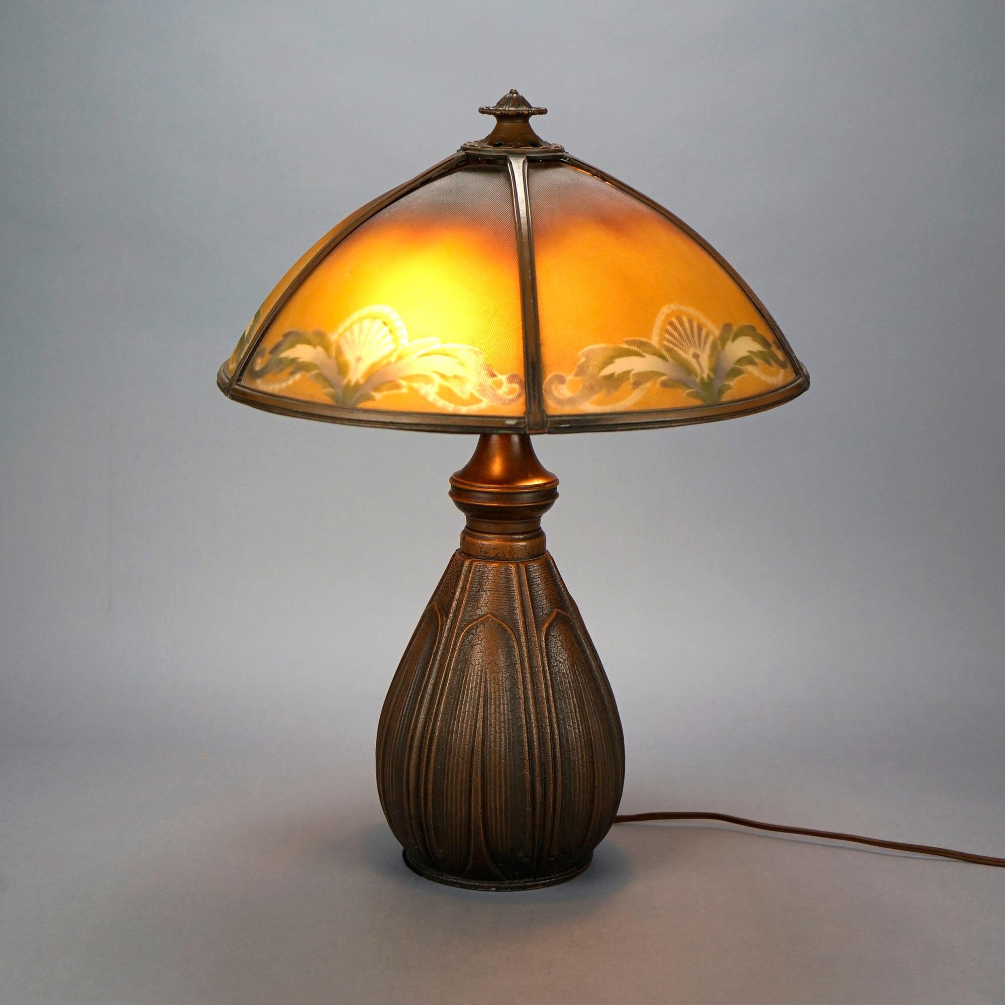 An antique Arts & Crafts table lamp by Bradley & Hubbard offers domed shade with reverse painted ribbed glass panels having foliate and stylized sunburst design surmounting double socket bulbous base having repeating pattern of stylized leaves,